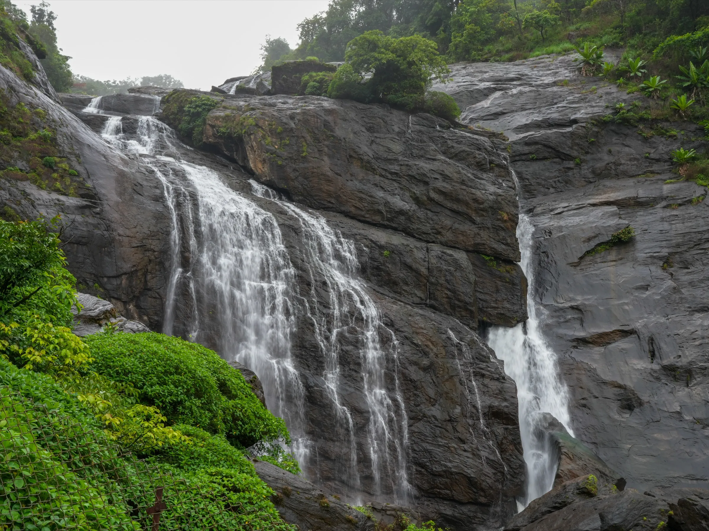 Upper section of Mallalli Falls pouring over dark rock in the monsoon; the trek passes the head of these falls