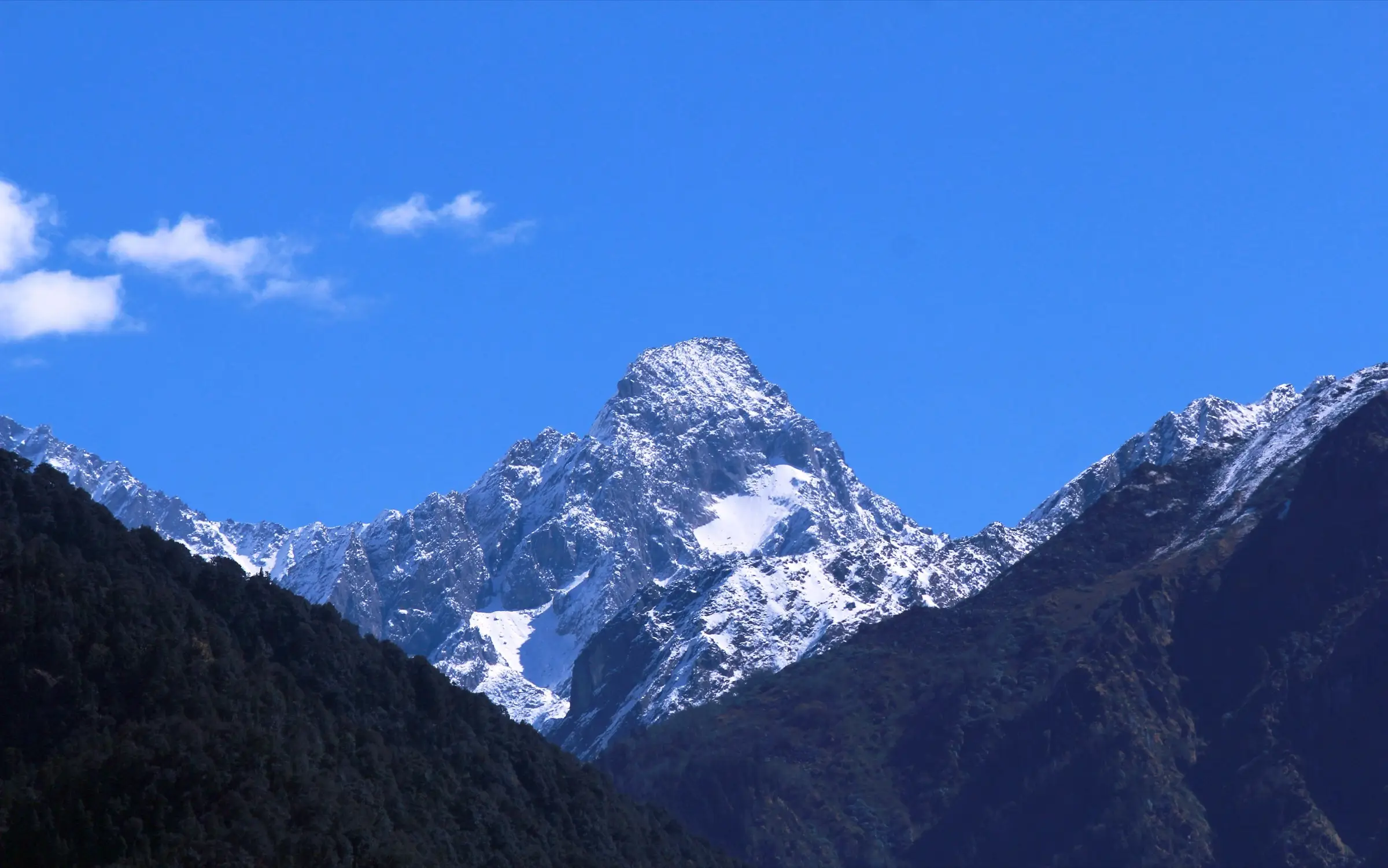 Snow-dusted Mandani peak rising between dark forested ridges, seen from the trail above Bantoli