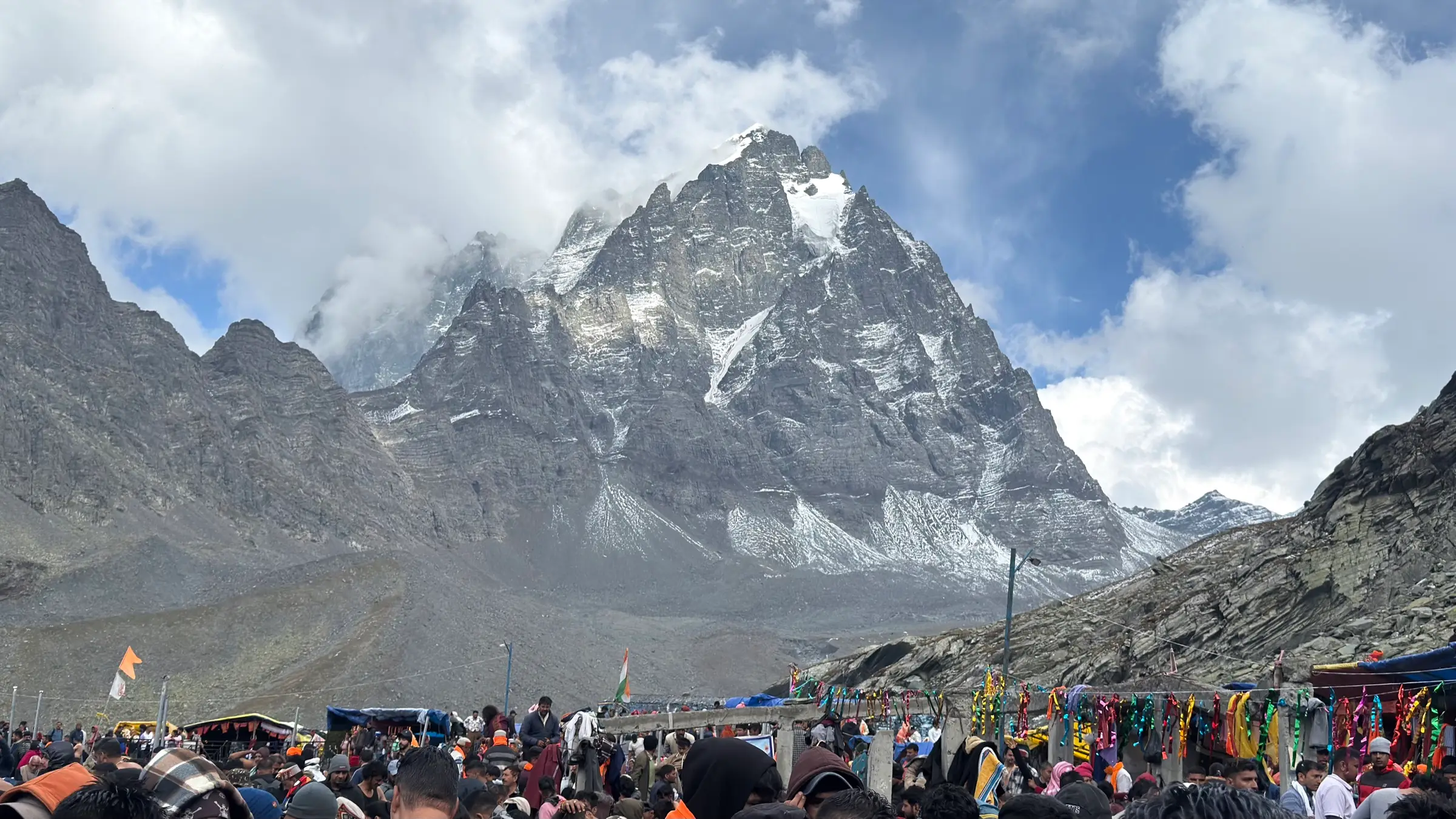 Crowds of yatris below the snow-streaked Manimahesh Kailash peak under clouds