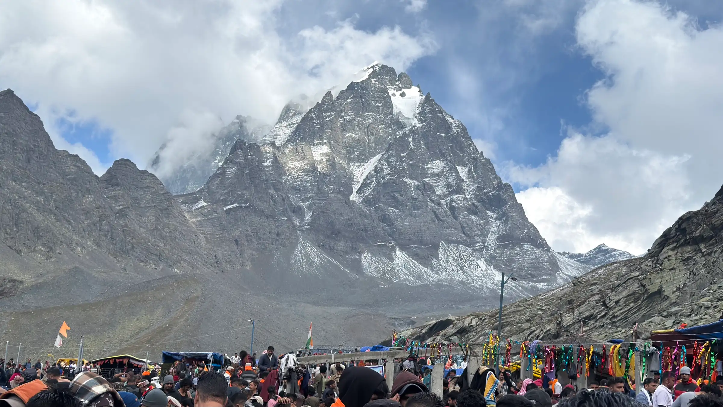 Crowds of yatris below the snow-streaked Manimahesh Kailash peak under clouds
