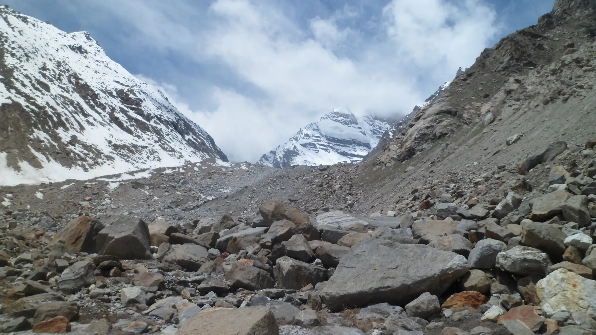 Boulder-strewn moraine near Mantalai with snow-covered peaks rising into cloud at the head of the Parvati valley