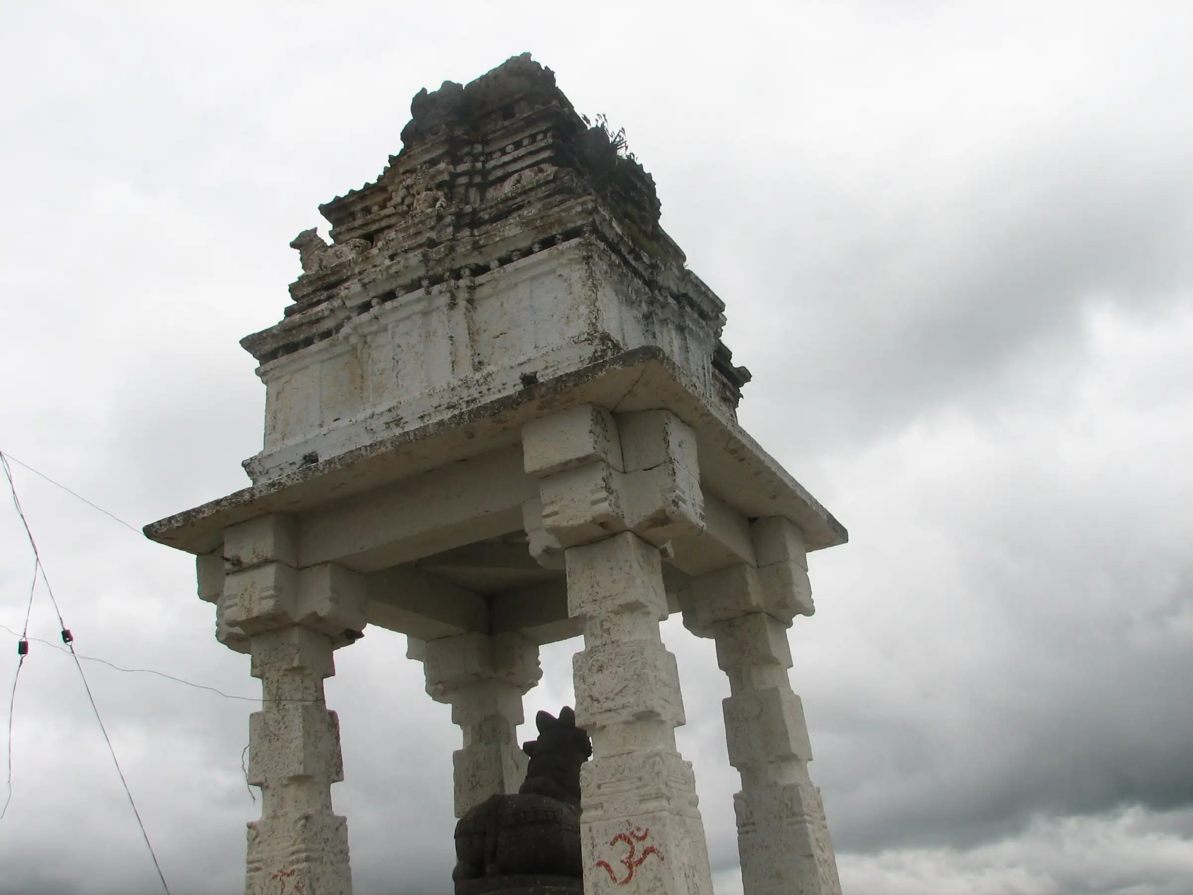 Stone mantapa with a carved tower over the Nandi on the summit of Savandurga, against a cloudy sky