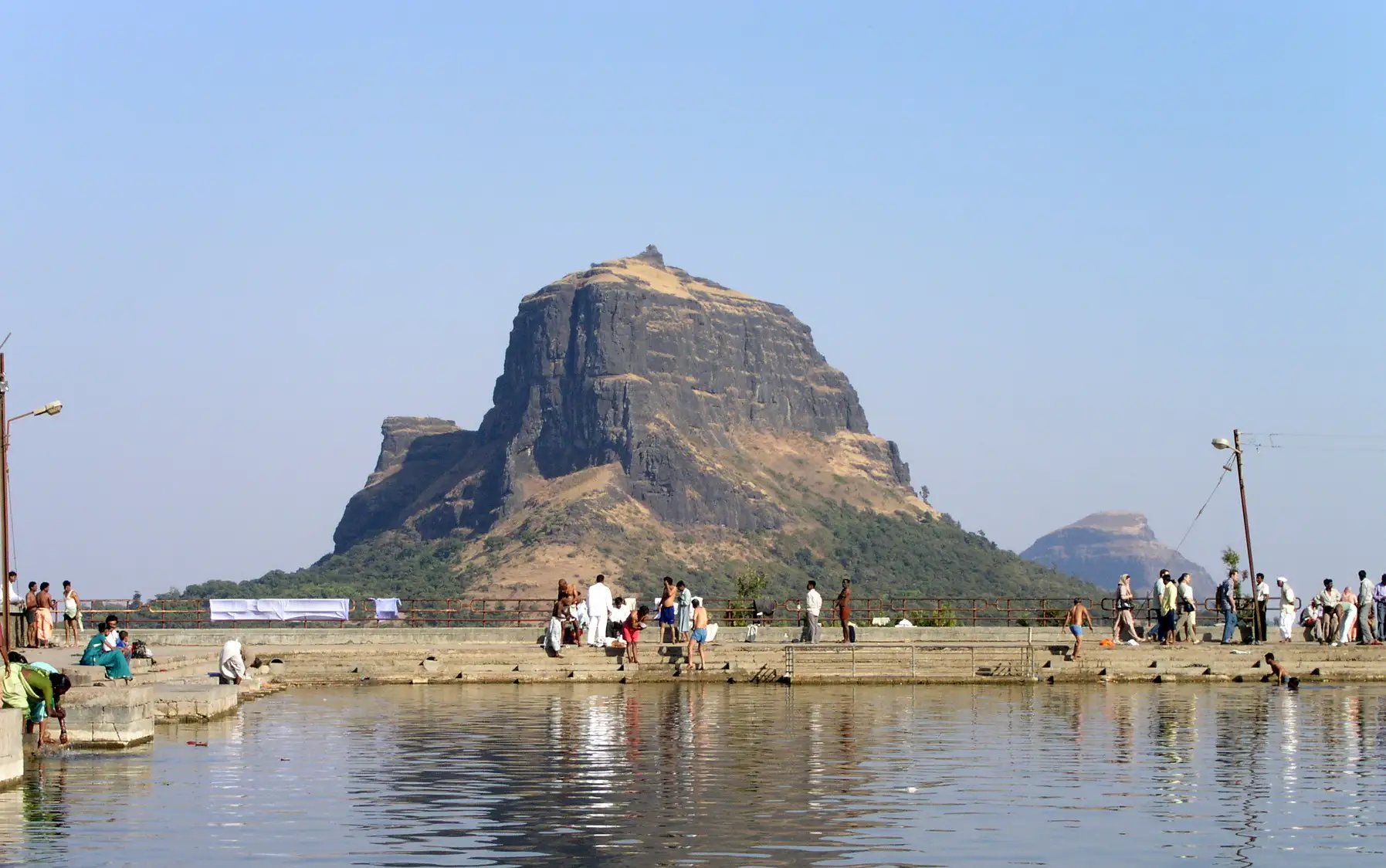 The dark basalt cliffs and pointed summit of Markandeya Fort seen across a pilgrims' bathing tank on Saptashrungi Gad