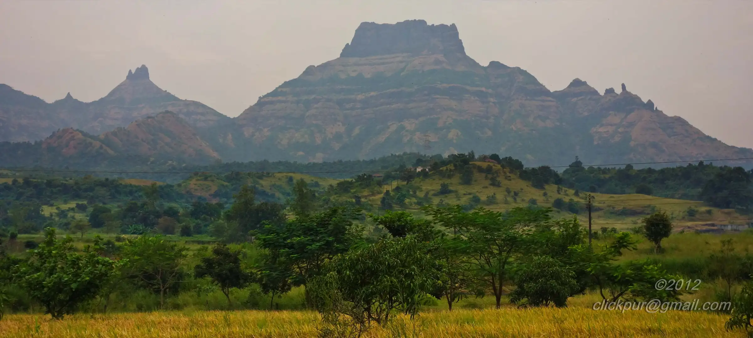 The flat-topped Chanderi massif with pinnacles on its ridge rising above green scrub and golden paddy fields on the Panvel side