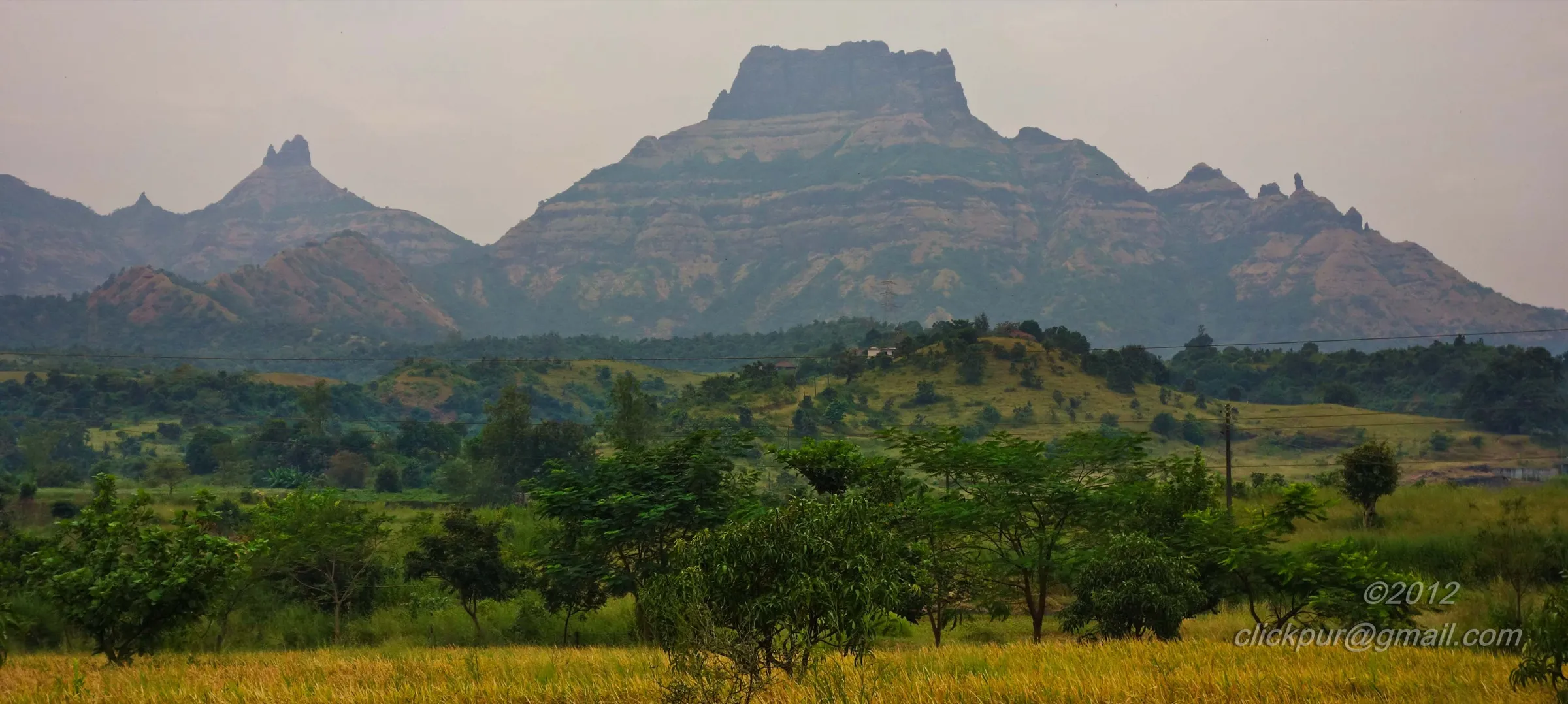 The flat-topped Chanderi massif with pinnacles on its ridge rising above green scrub and golden paddy fields on the Panvel side
