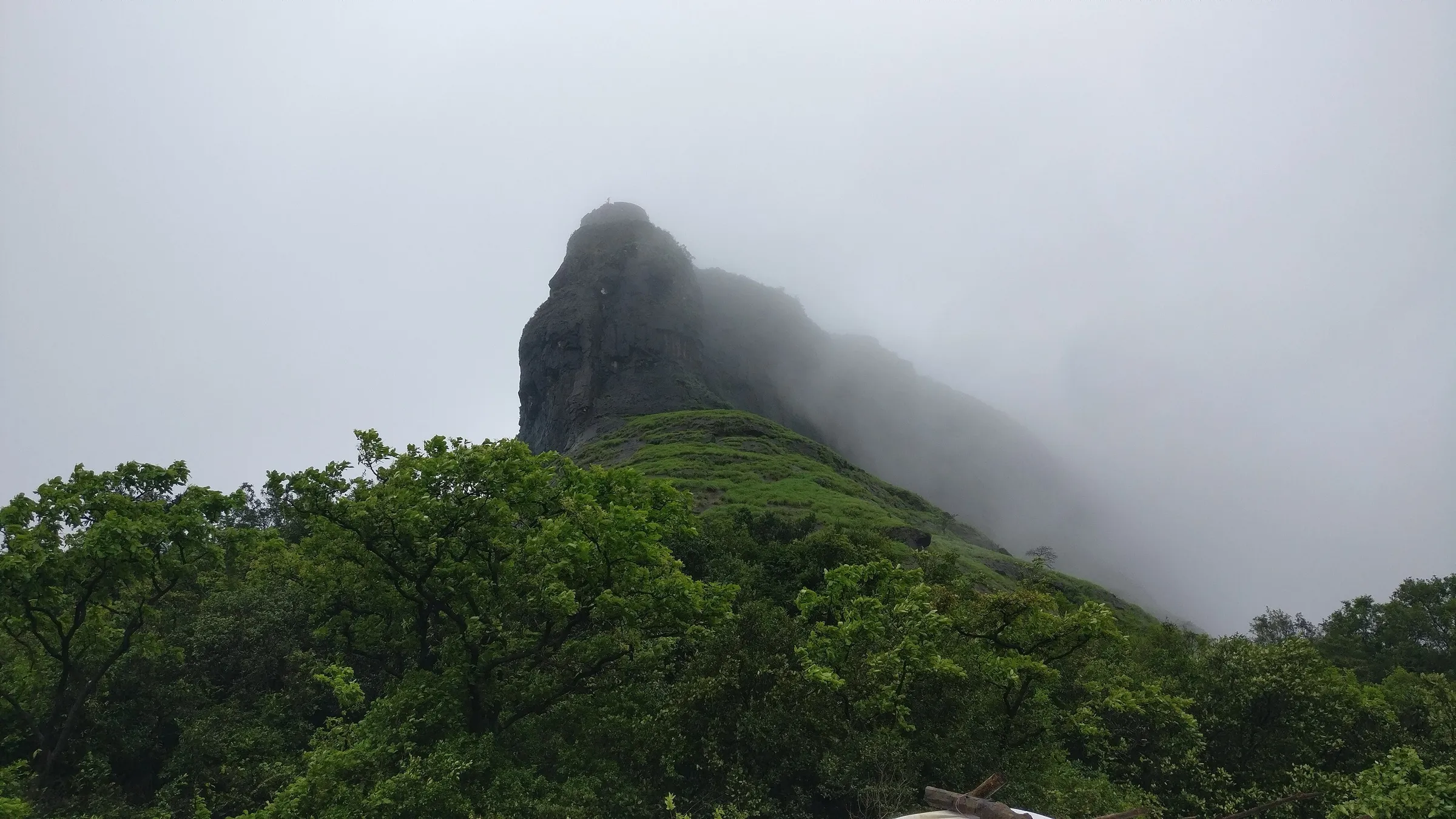 Rajmachi fort hill wrapped in green monsoon slopes and cloud, seen from the trail