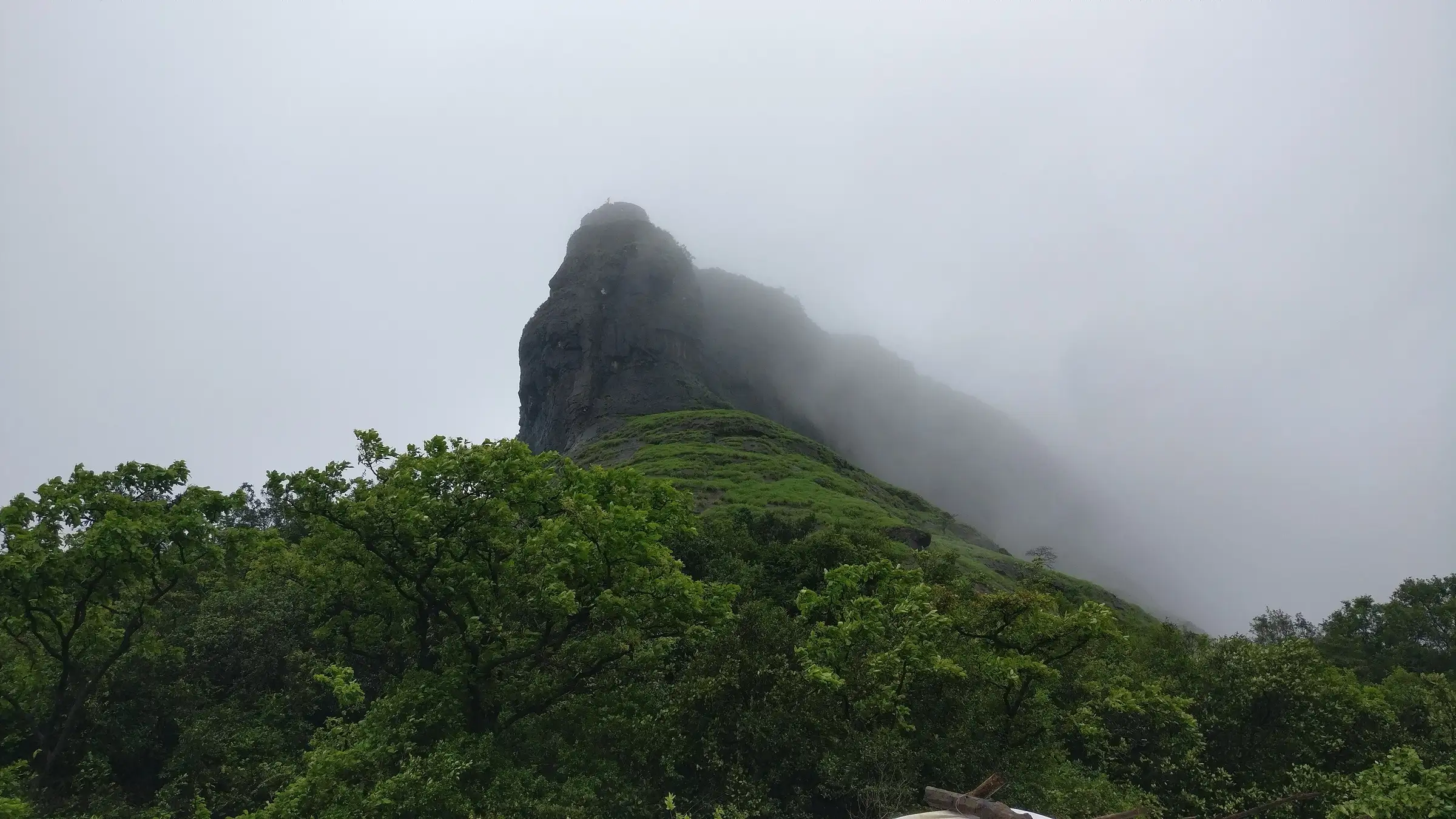 Rajmachi fort hill wrapped in green monsoon slopes and cloud, seen from the trail