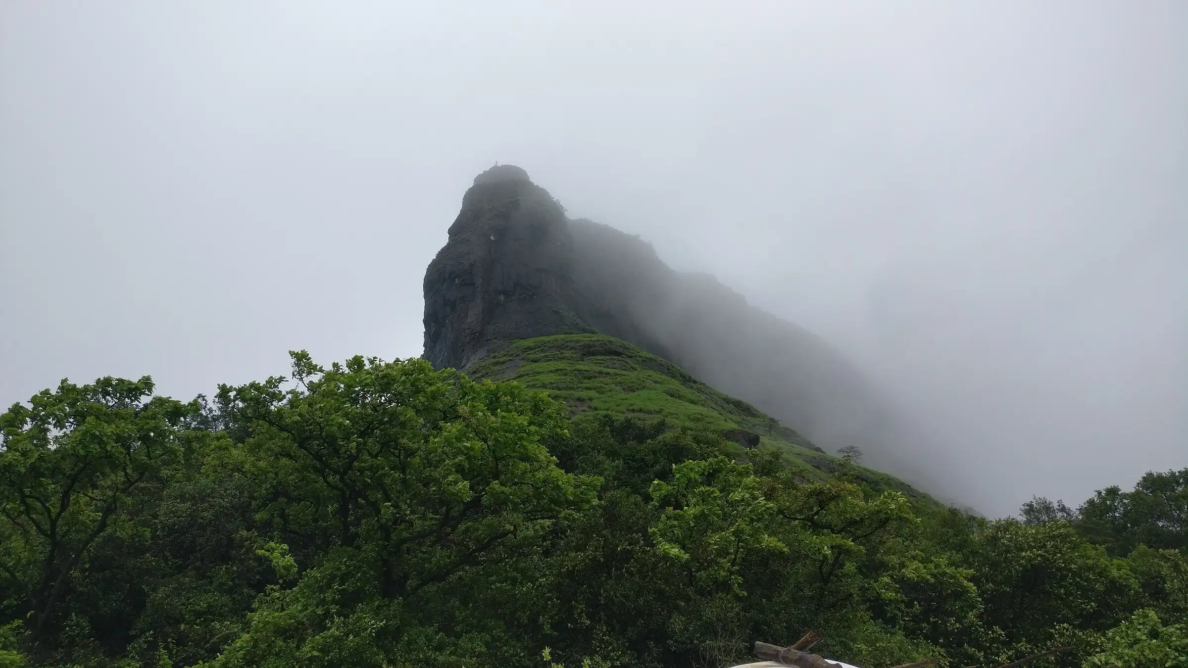Rajmachi fort hill wrapped in green monsoon slopes and cloud, seen from the trail