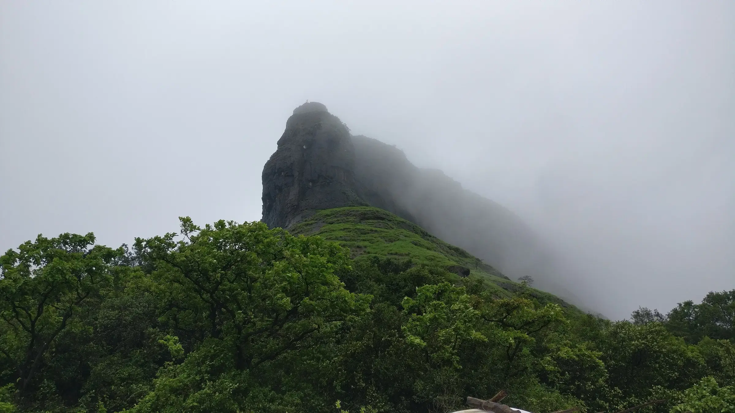 Rajmachi fort hill wrapped in green monsoon slopes and cloud, seen from the trail