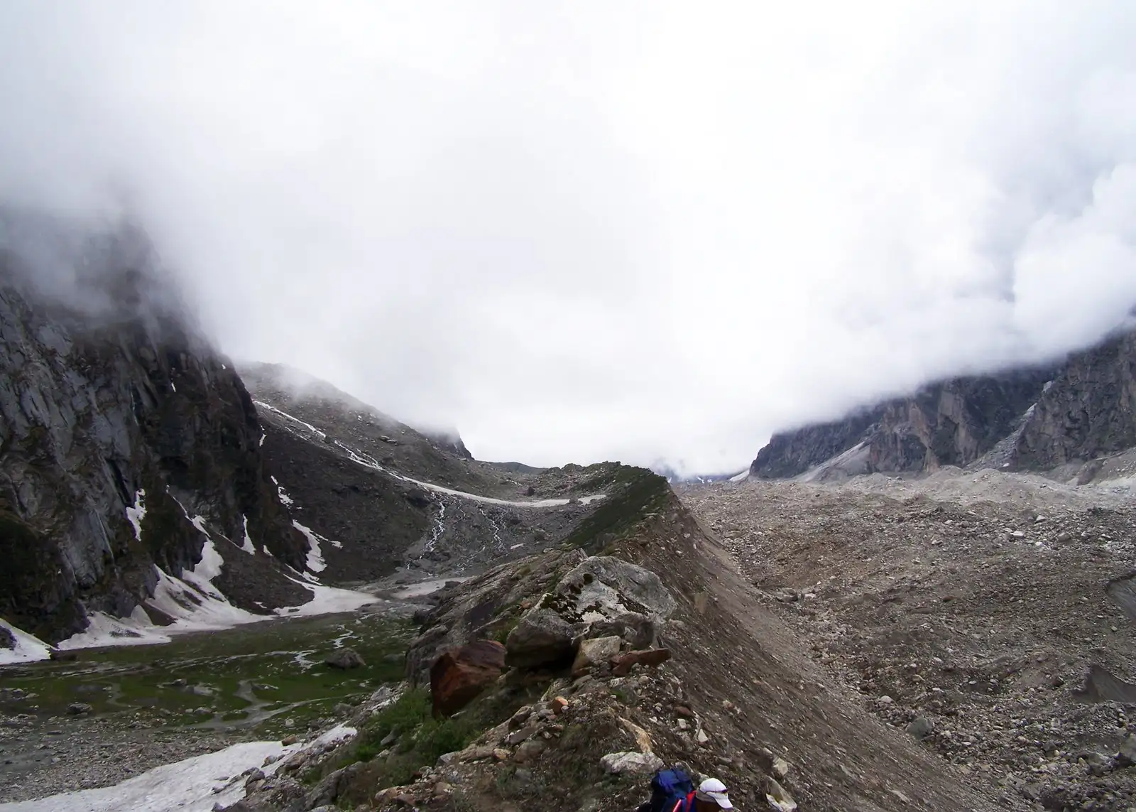 Trekkers on a narrow moraine ridge beside the Satopanth Glacier with cloud hanging over the valley