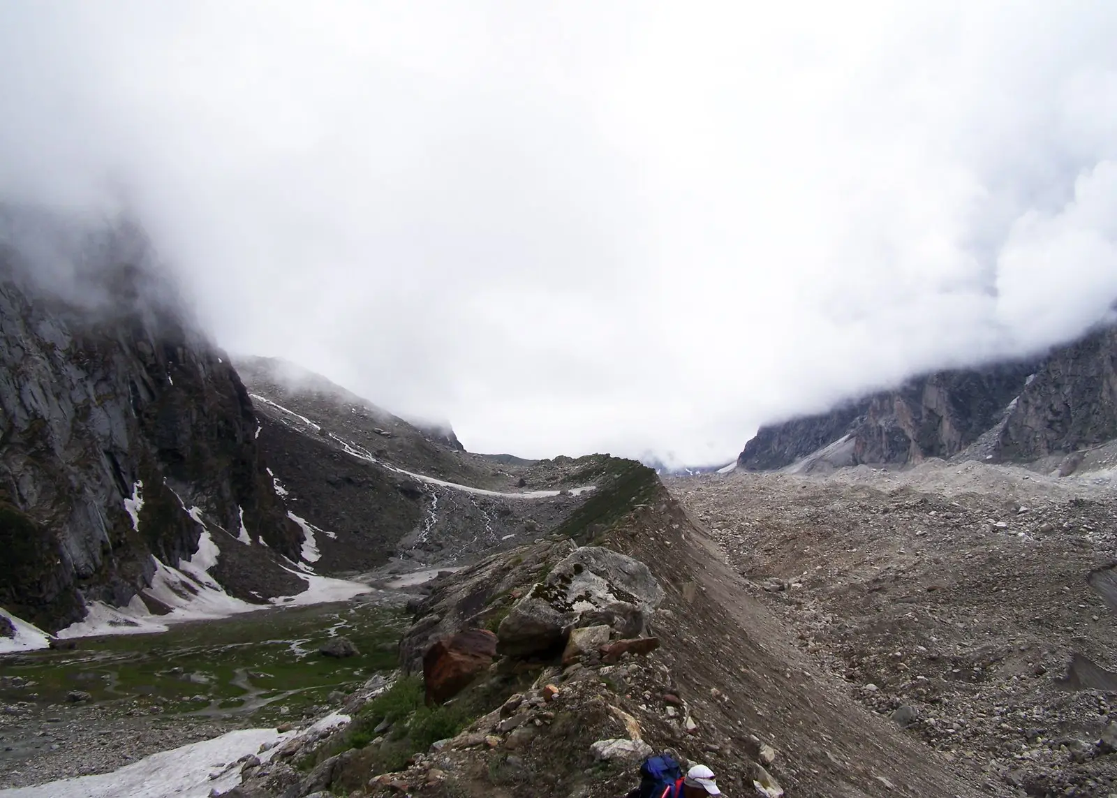 Trekkers on a narrow moraine ridge beside the Satopanth Glacier with cloud hanging over the valley
