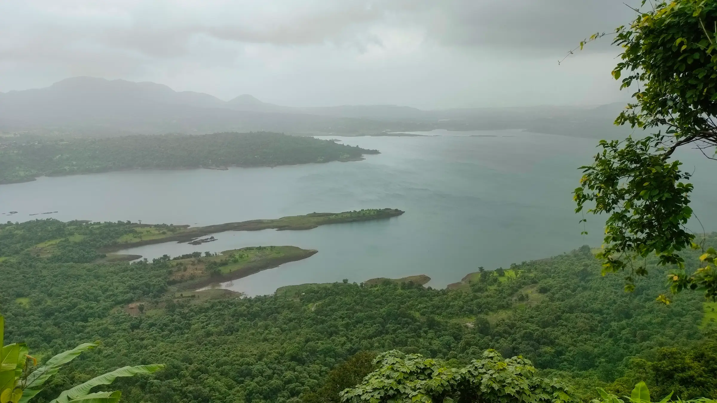 Morbe Dam reservoir and forested islands seen from the slopes of Irshalgad on a cloudy day
