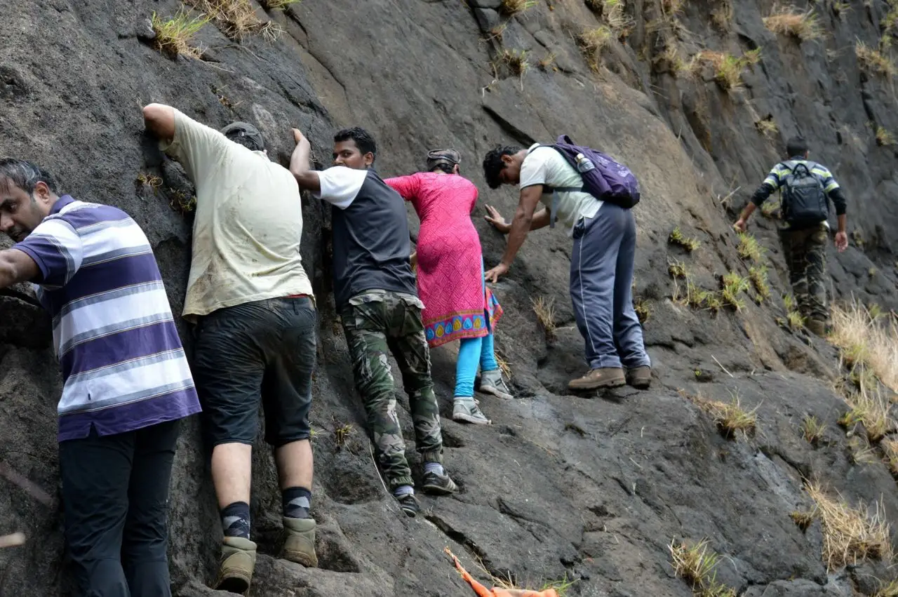 Trekkers edging along a sloping rock ledge on the way to the cave on Mrugagad