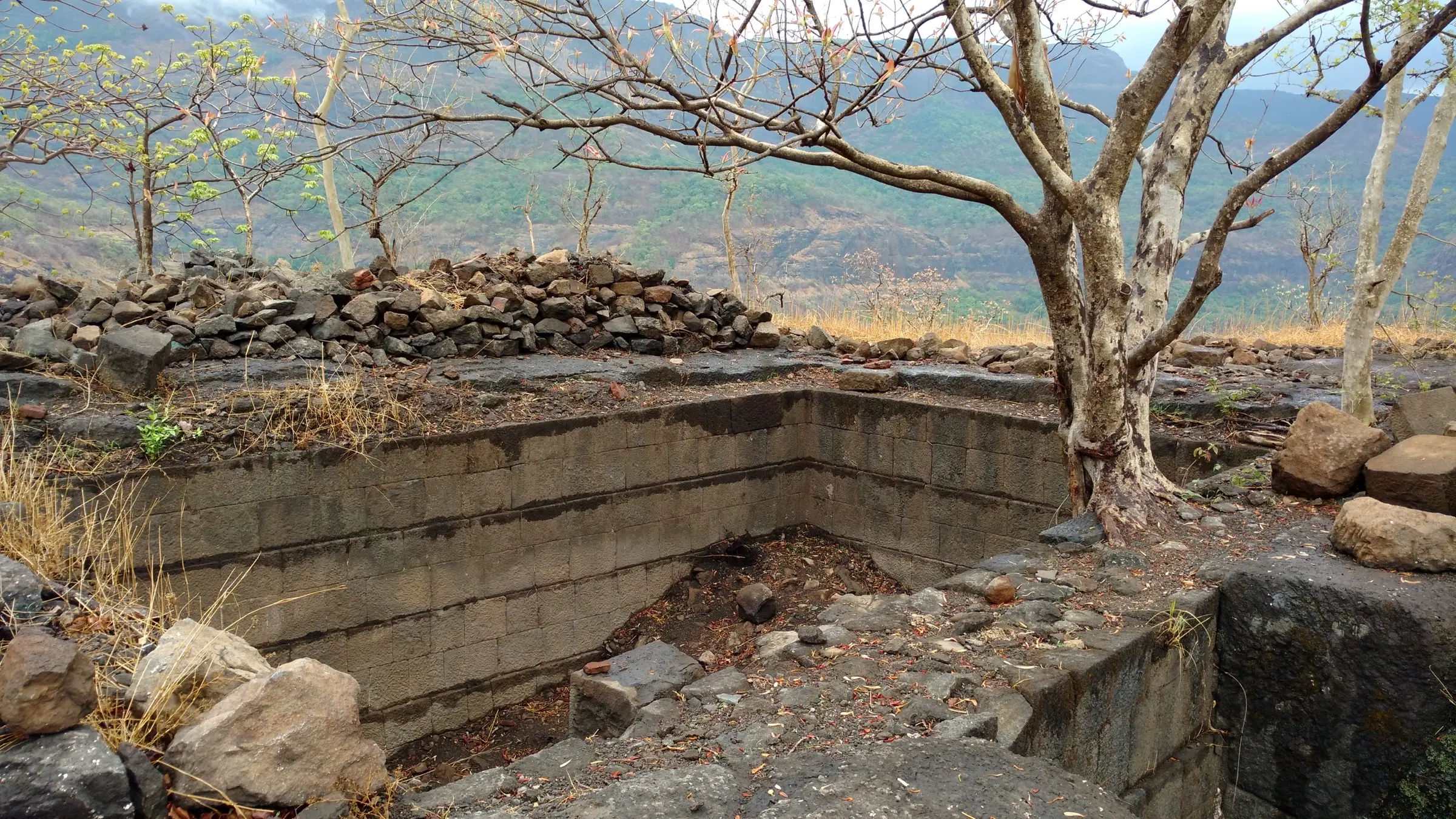 A dry stone-lined water tank on the top of Mrugagad with the Sahyadri slopes behind