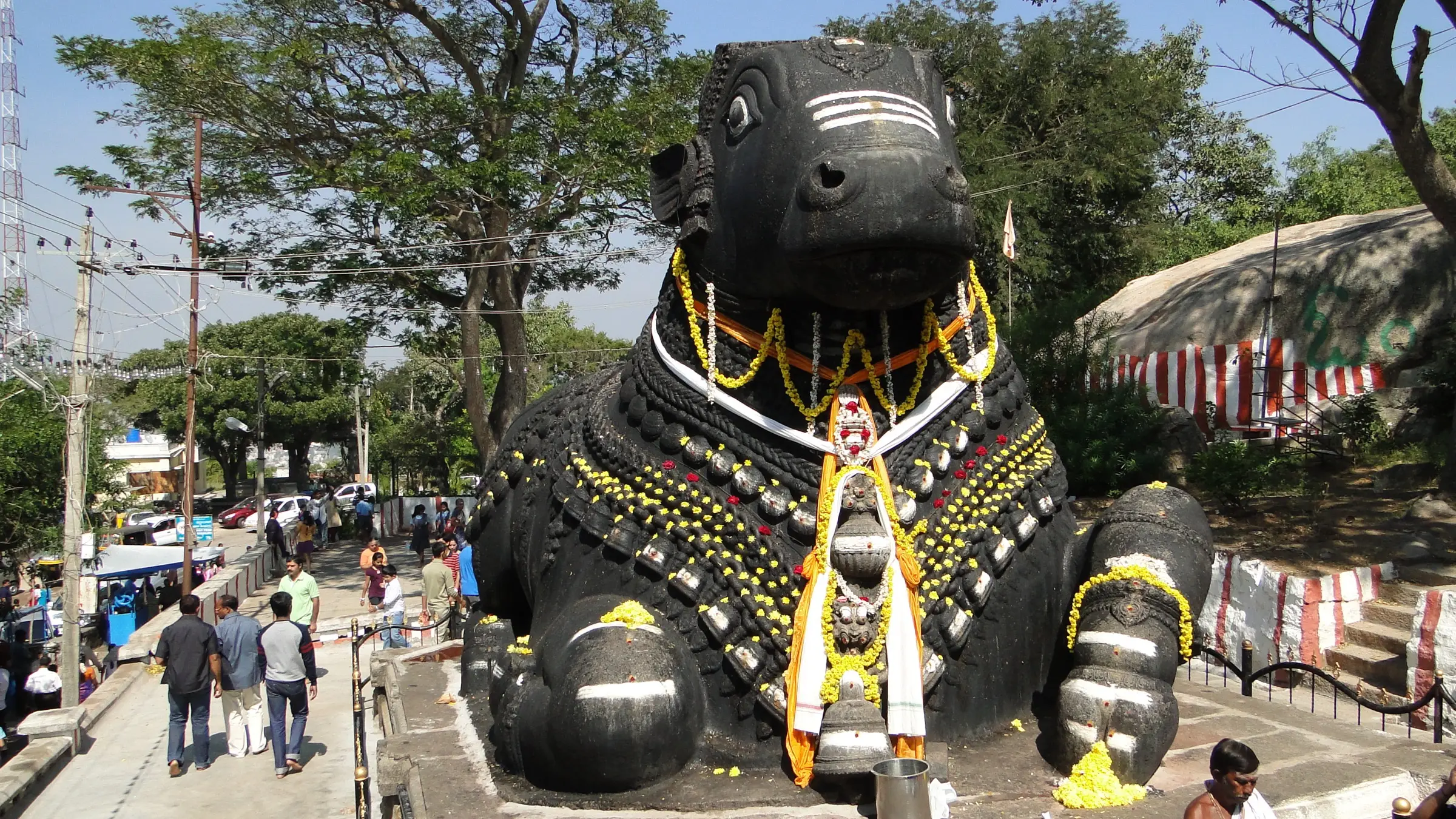 The giant black granite Nandi on Chamundi Hill, decorated with garlands and bells, with visitors on the path beside it