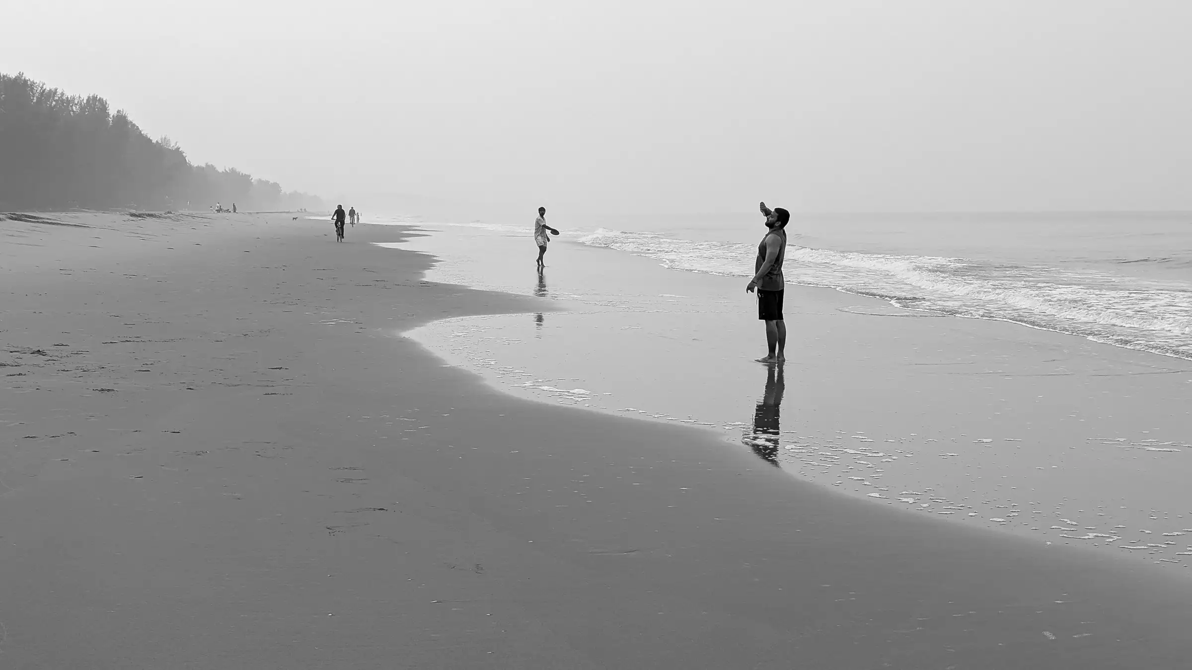 Black-and-white view of people walking along the long, empty sand of Nirvana Beach in morning haze