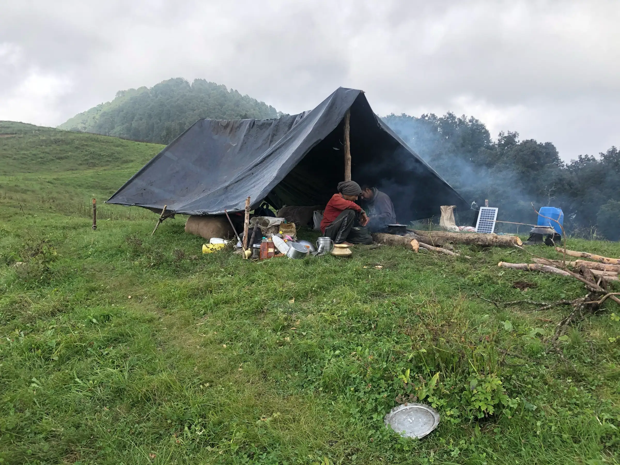 A herder's tarpaulin shelter with cooking pots and a small solar panel on the Panwali Kantha grassland under cloud