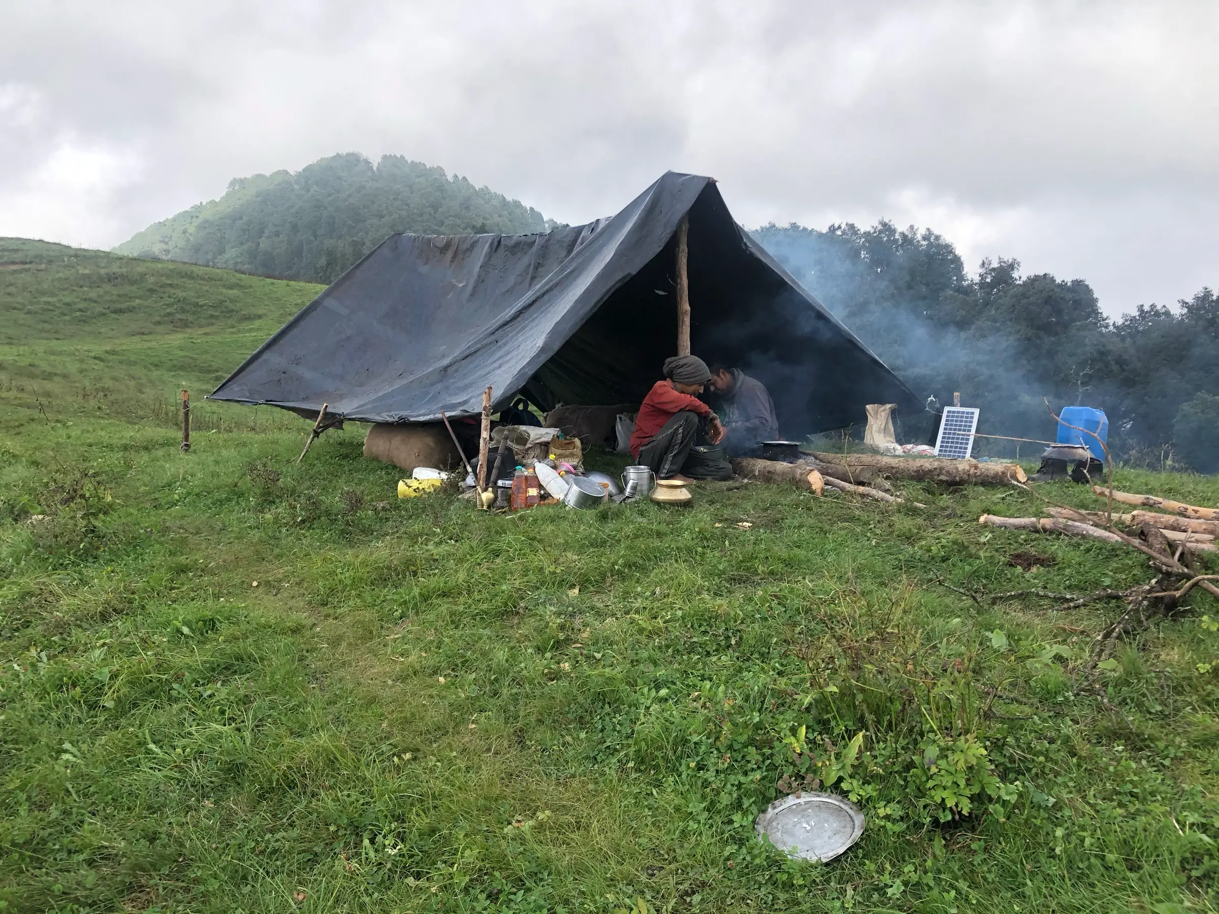 A herder's tarpaulin shelter with cooking pots and a small solar panel on the Panwali Kantha grassland under cloud