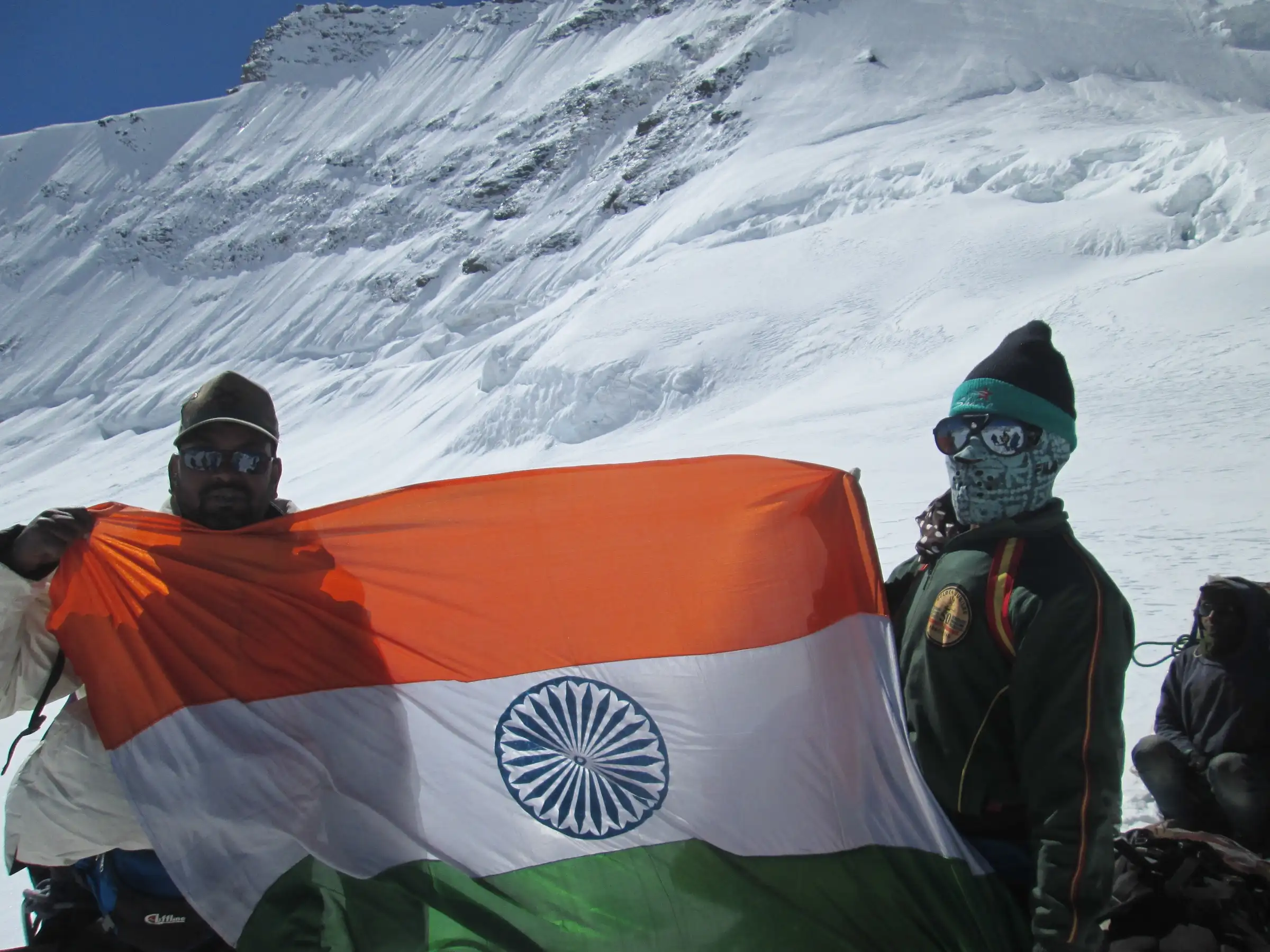 Trekkers holding the Indian flag on the snowy Kalindi Khal pass in front of a glaciated slope