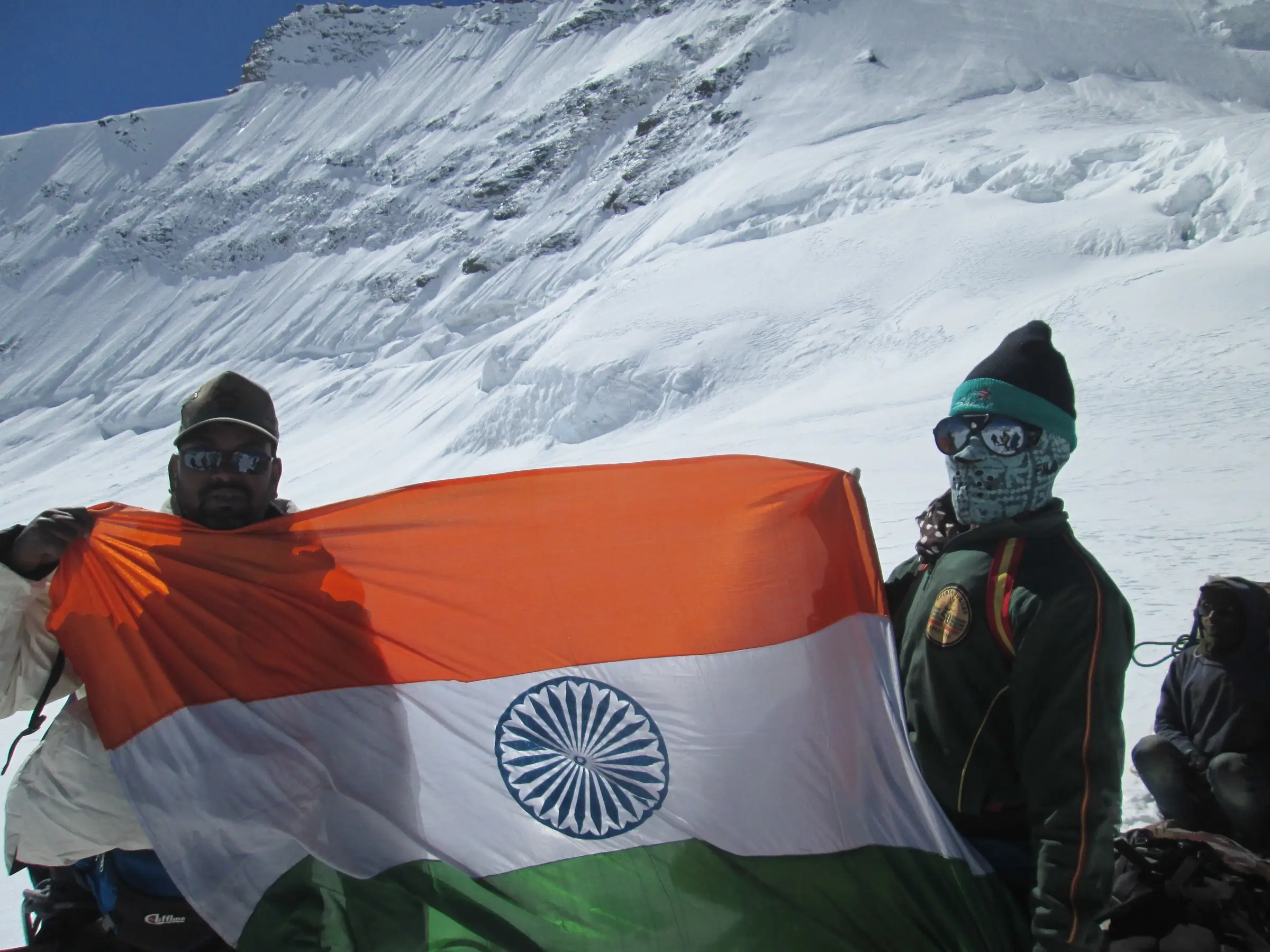 Trekkers holding the Indian flag on the snowy Kalindi Khal pass in front of a glaciated slope
