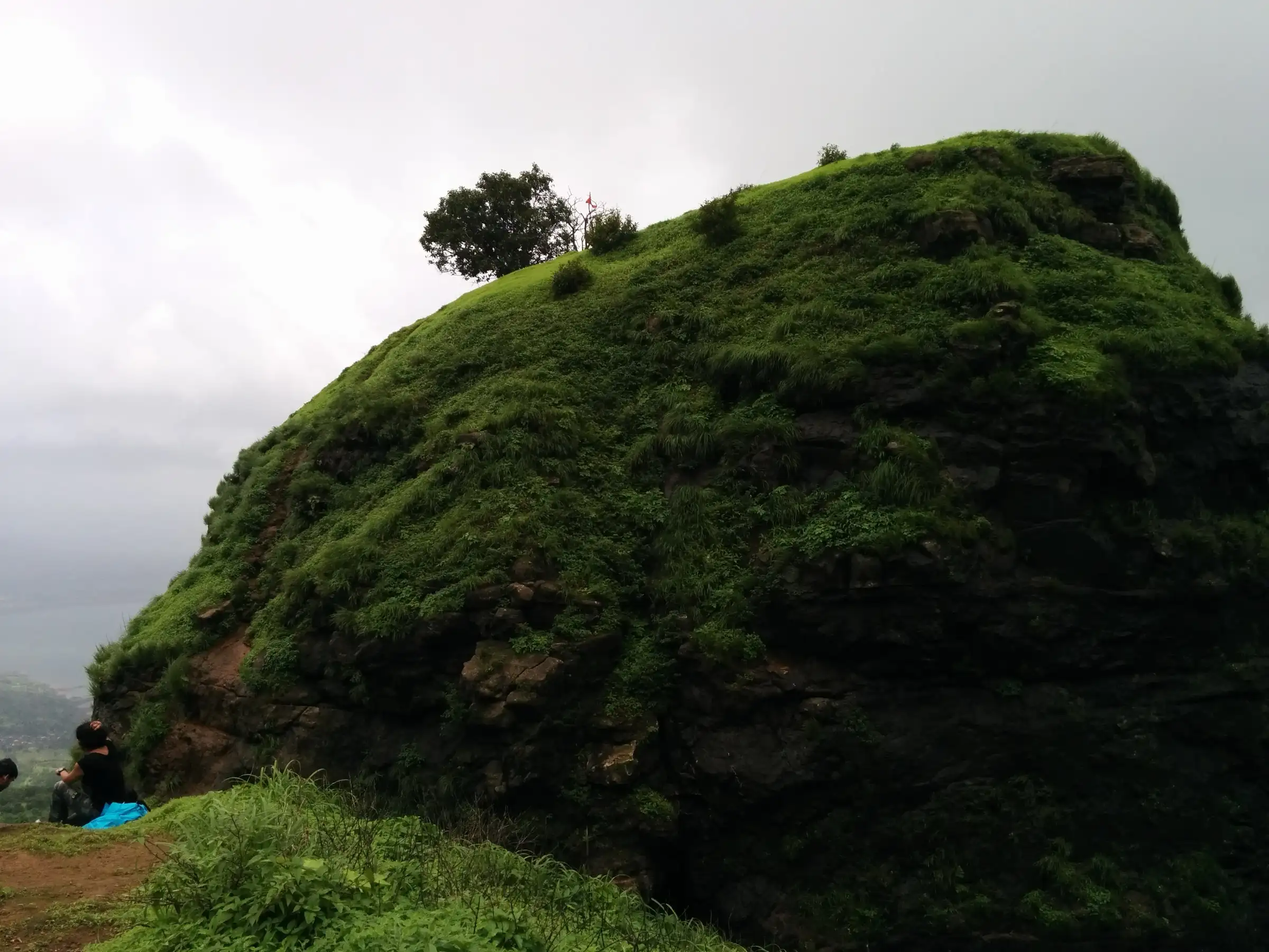 The grassy knoll of One Tree Hill with its single tree on top, seen from the Matheran ridge in the monsoon with trekkers resting at the edge