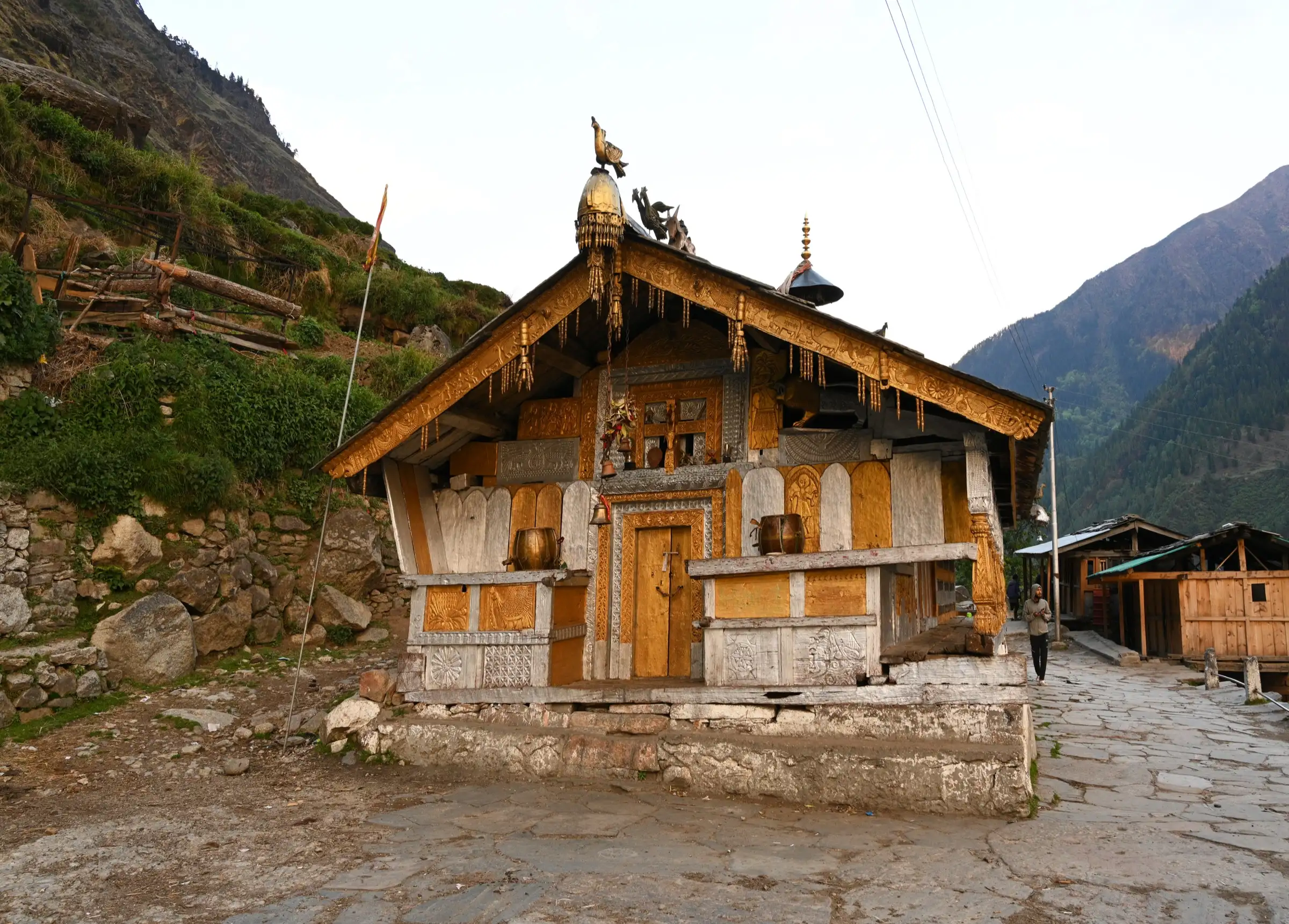 Carved wooden temple with brass ornaments on a stone-paved lane in Osla village, passed on the way down from the lake