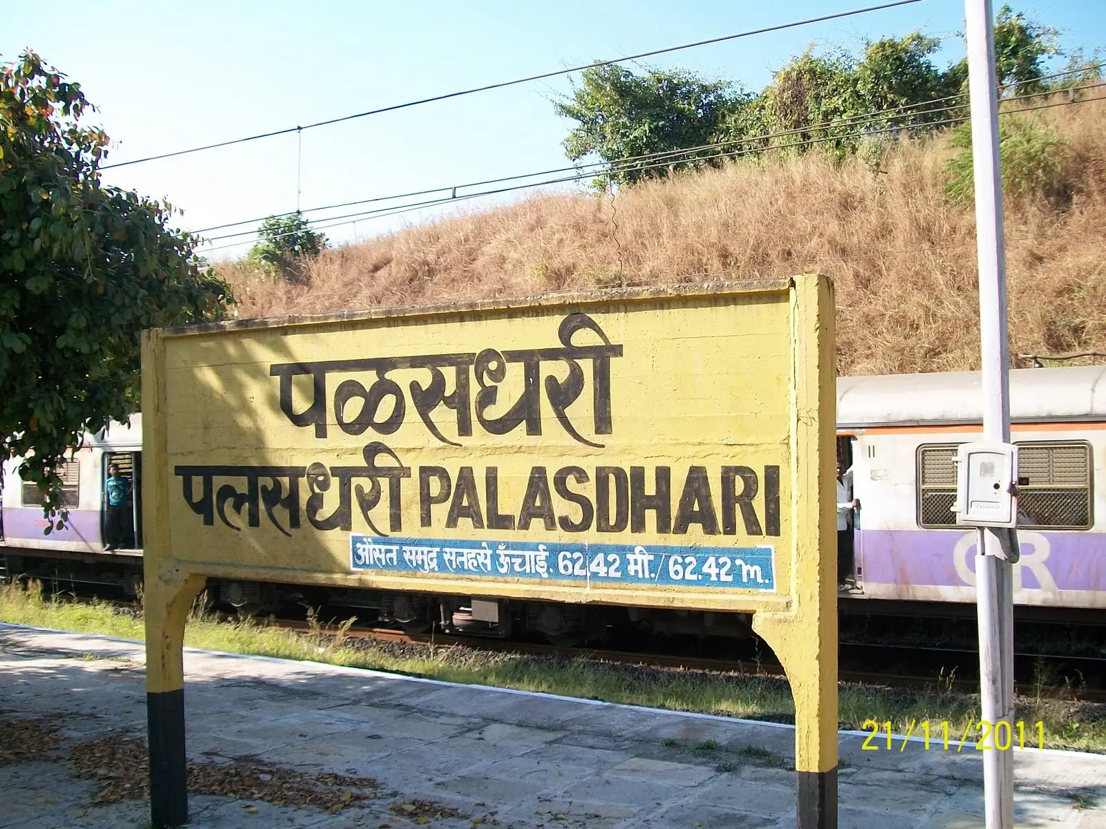Palasdhari railway station board, the starting point for the trek, with a dry grassy slope behind