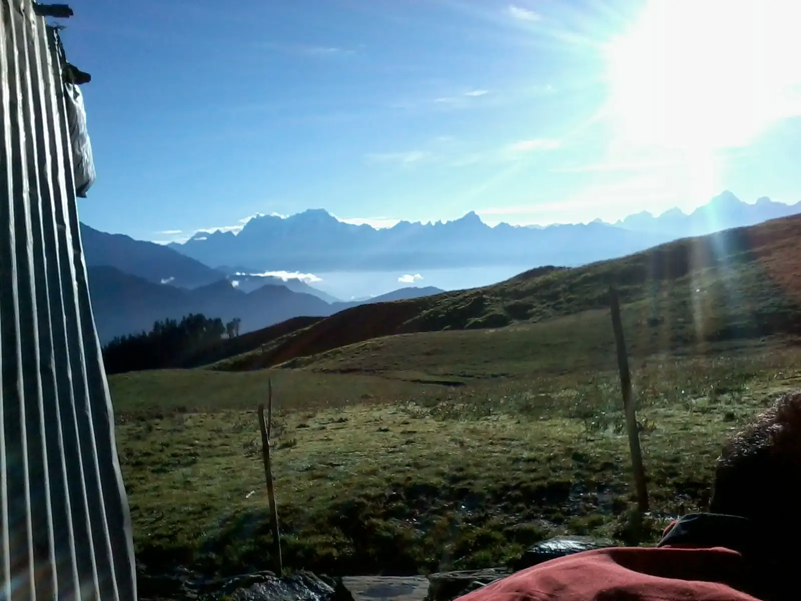 Morning sun over the green Panar Bugyal meadow with a line of snow peaks beyond, seen from a hut on the way to Rudranath