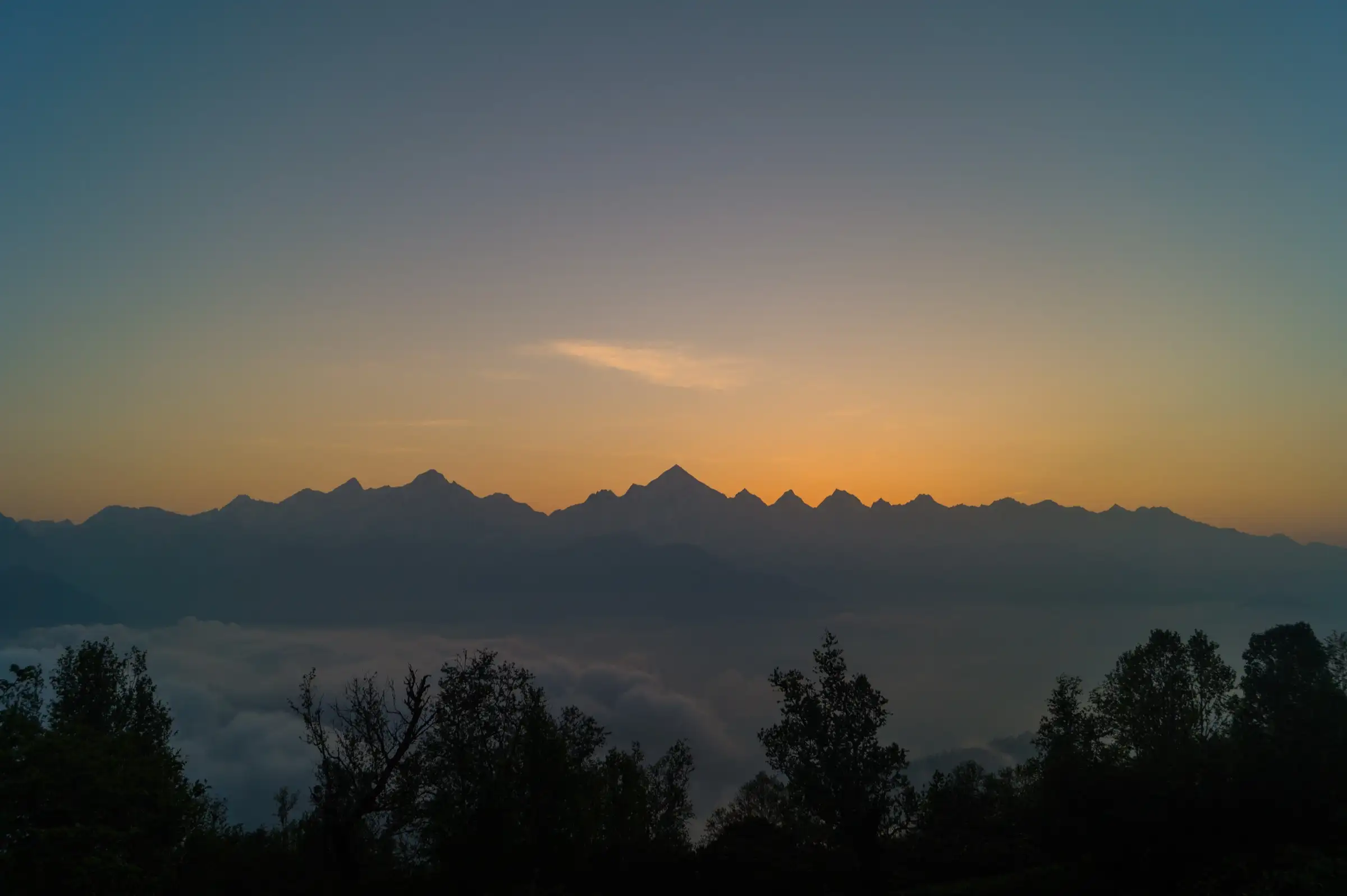 The Panchachuli range in silhouette at dawn above a sea of cloud and forest, seen from near Munsiyari