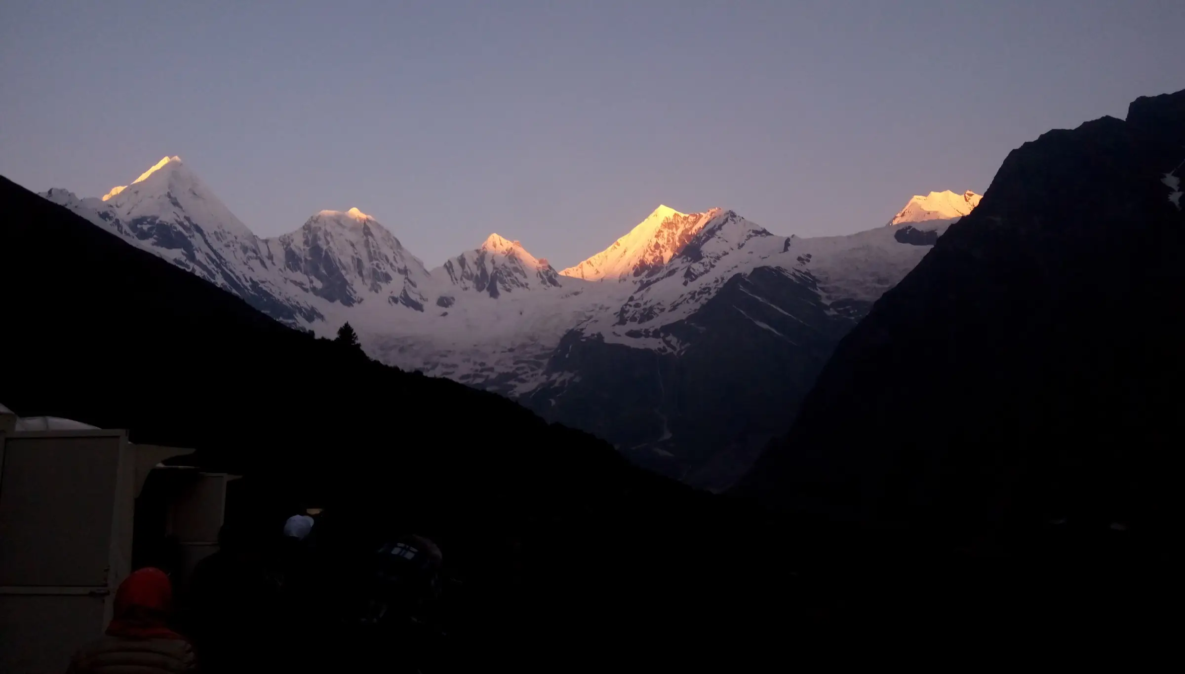 First sunlight on the five snow-covered Panchachuli peaks above a dark valley, seen from the Darma valley