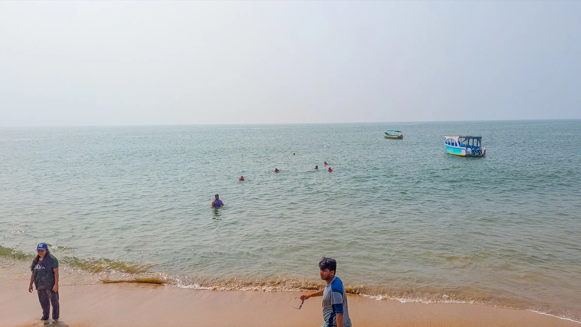 Swimmers and boats in calm water off Paradise Beach, Gokarna, with walkers on the sand