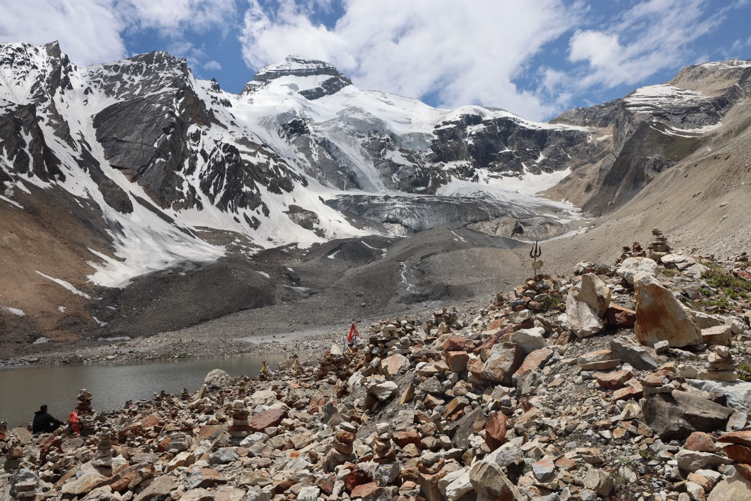 Parvati Kund lake at Jolingkong with stone cairns and a trident in the foreground and the glaciated Adi Kailash massif behind