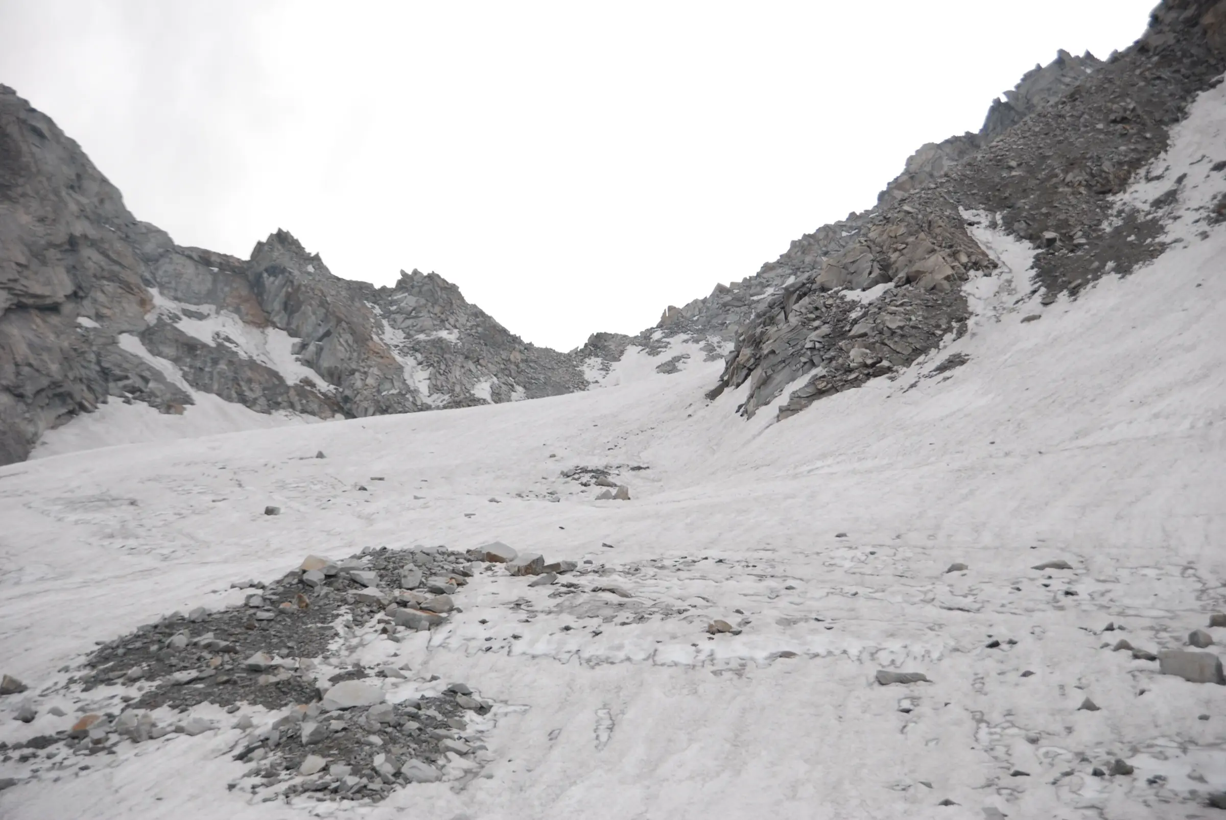 Snow-covered glacier with scattered rocks rising to Borasu Pass between grey rocky ridges