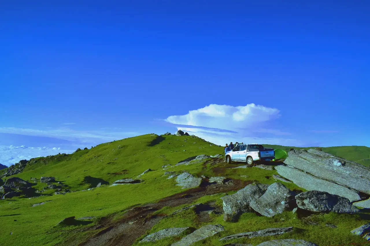 A pickup truck parked on the grassy, rocky top of Chanshal Pass above a sea of clouds