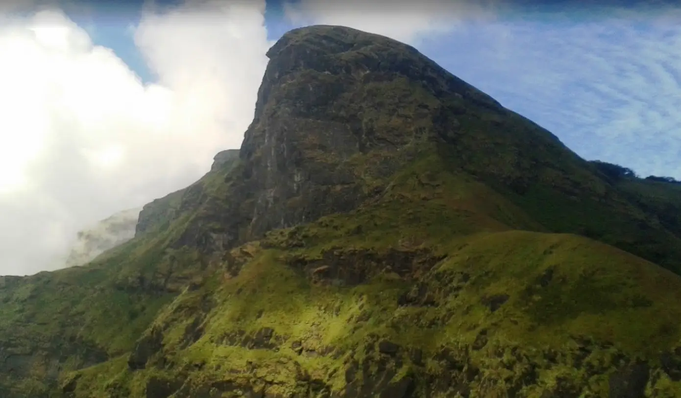 The dark rocky 'horse face' of Kudremukh peak above grassy slopes, with cloud rising on the left