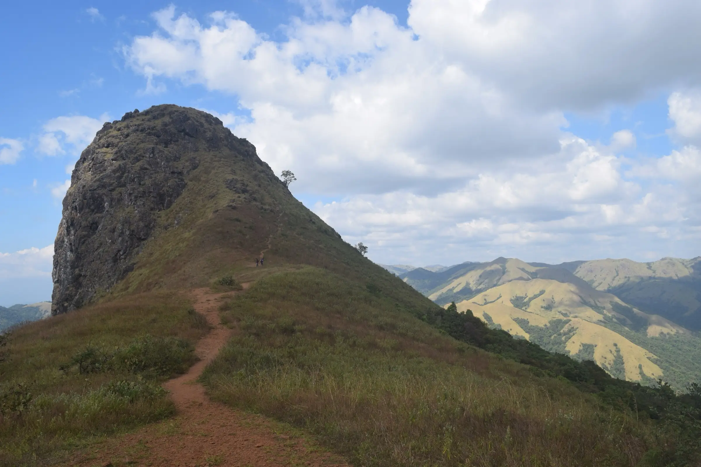 Trail across grassland leading to the rocky hump of Ettina Bhuja, with the Charmadi hills behind