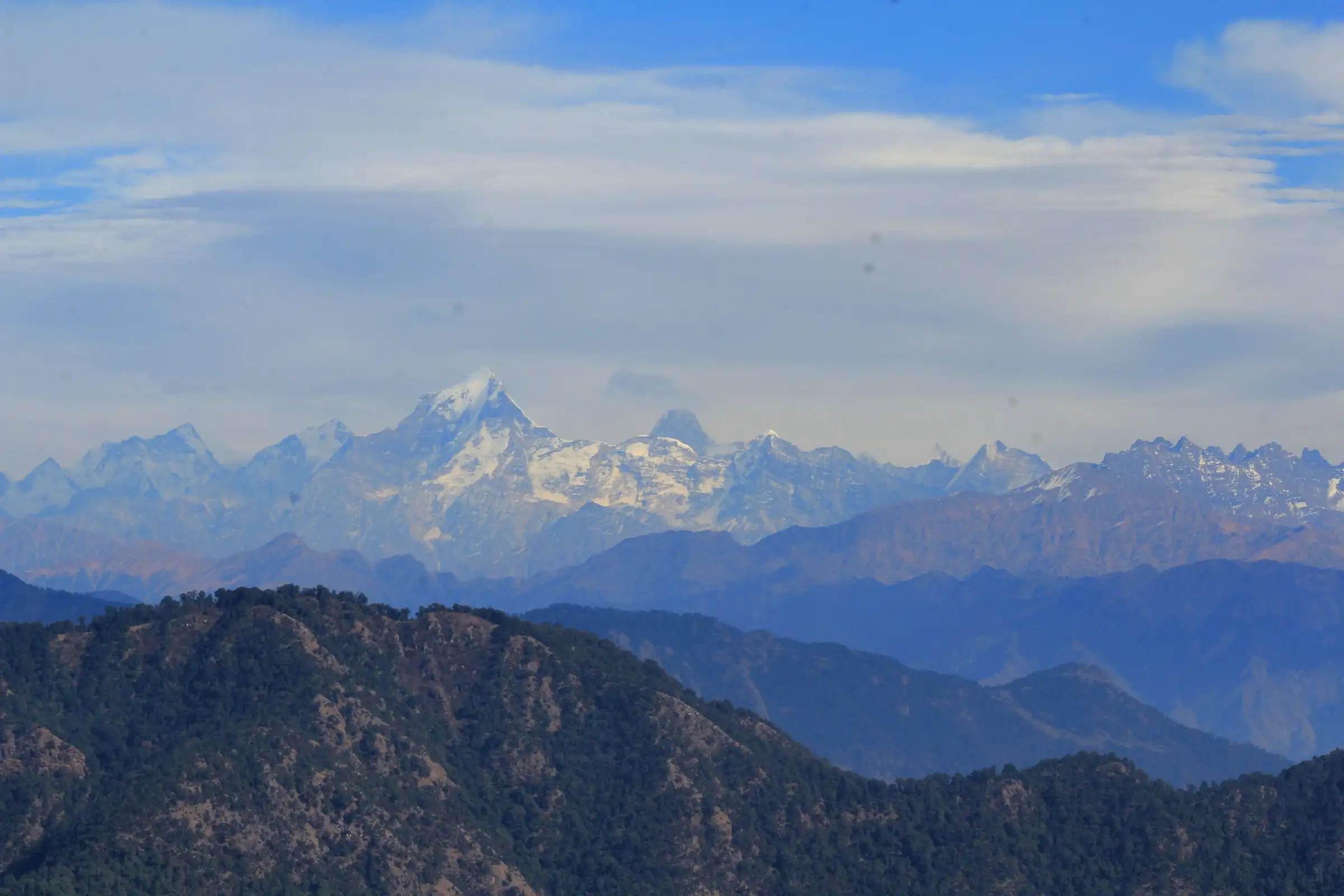 Snow peaks of the Garhwal Himalaya rising beyond forested ridges, seen from Kartik Swami Temple
