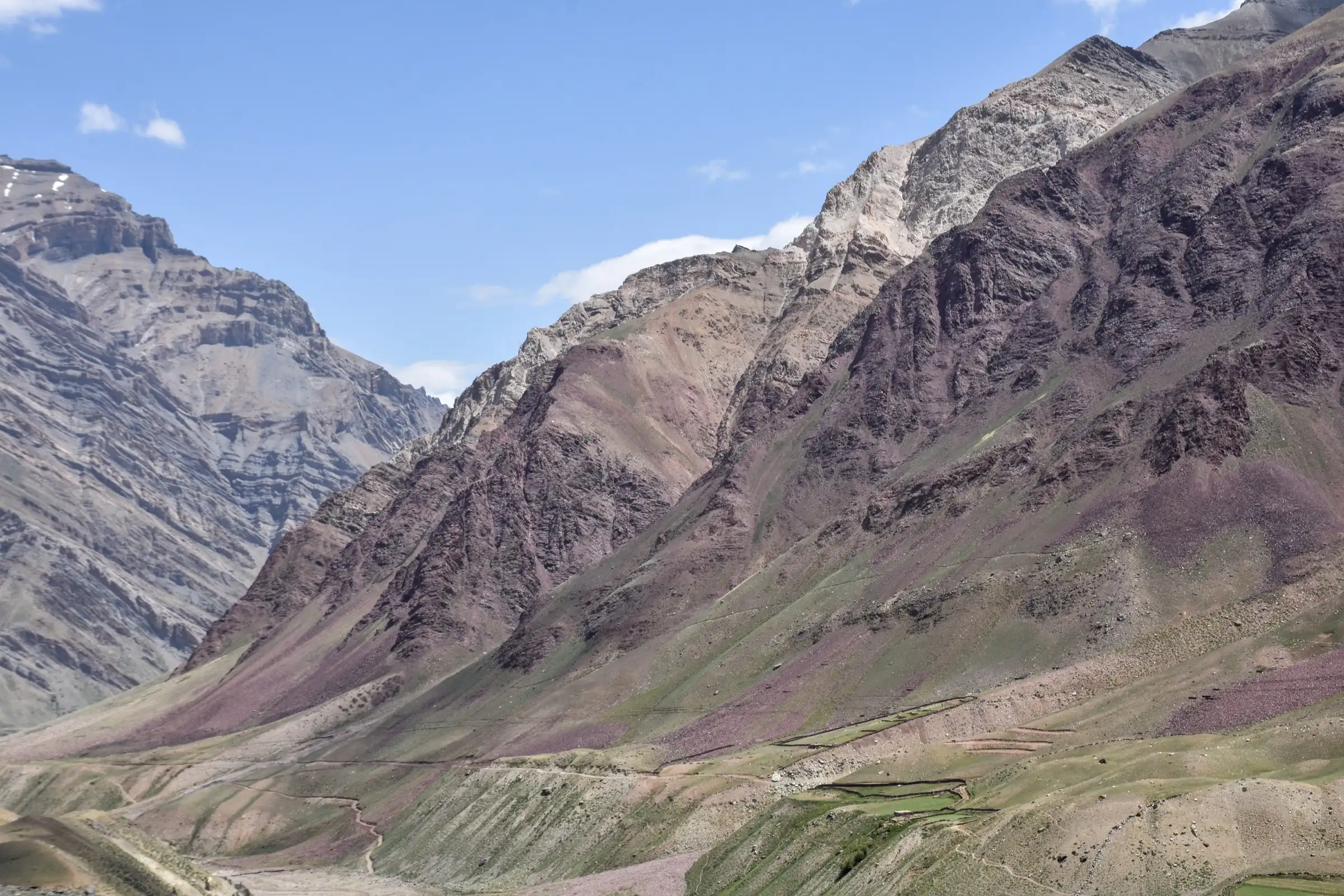 Bare, banded rock slopes with sparse alpine vegetation on the right bank of the Pin River opposite Mudh, in the valley the Larsa We trek descends into (not the trek itself)