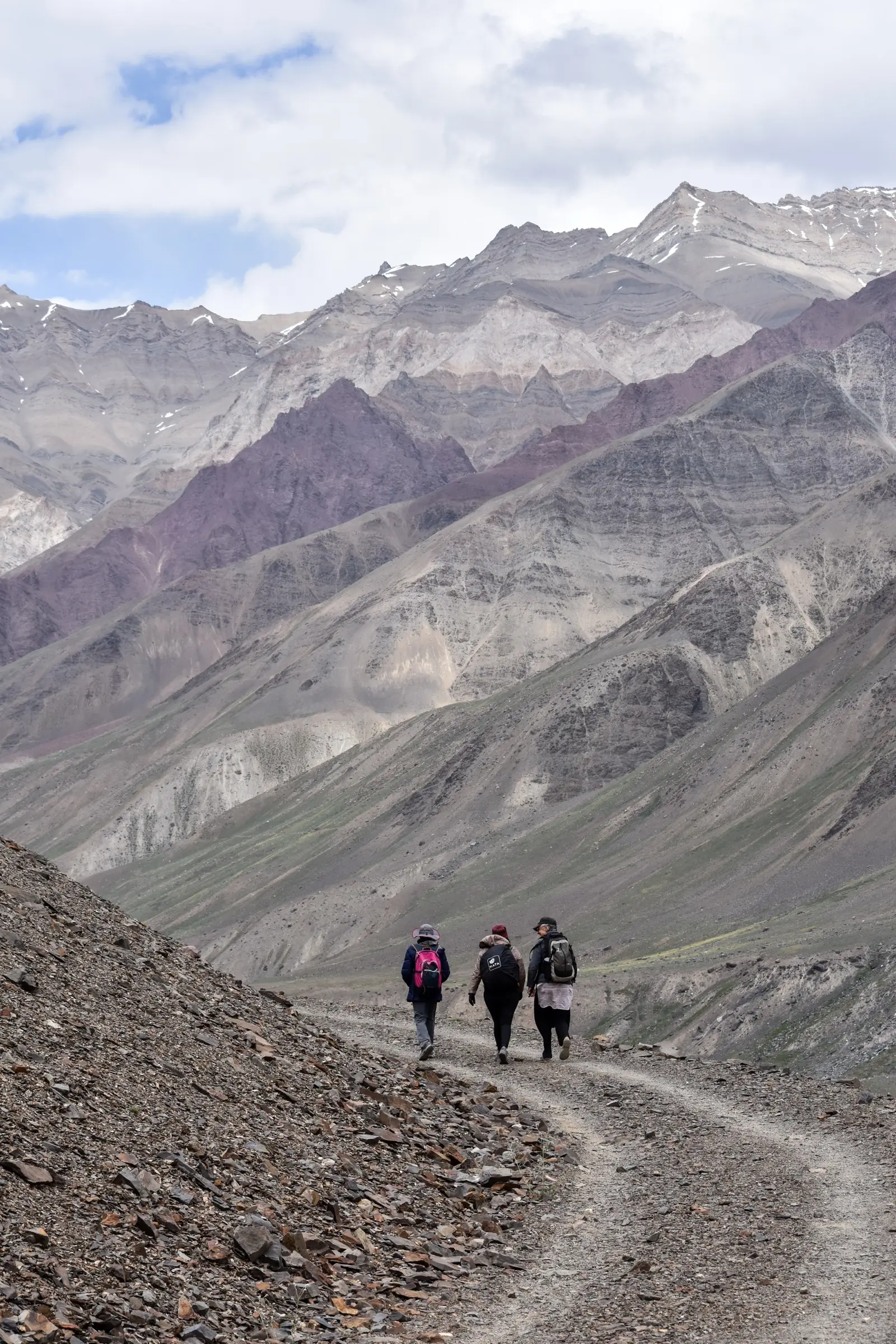 Three hikers on the trail along the Pin river towards Mudh, below bare banded mountains of Spiti
