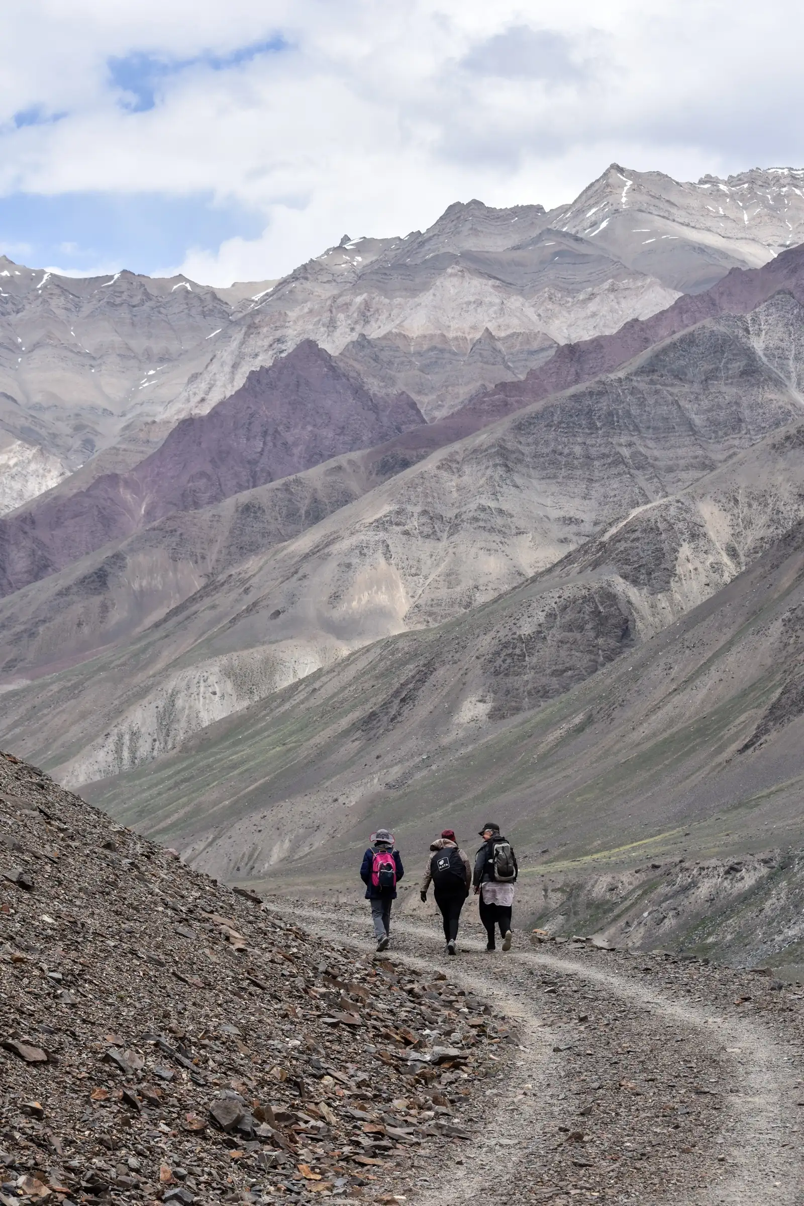 Three hikers on the trail along the Pin river towards Mudh, below bare banded mountains of Spiti