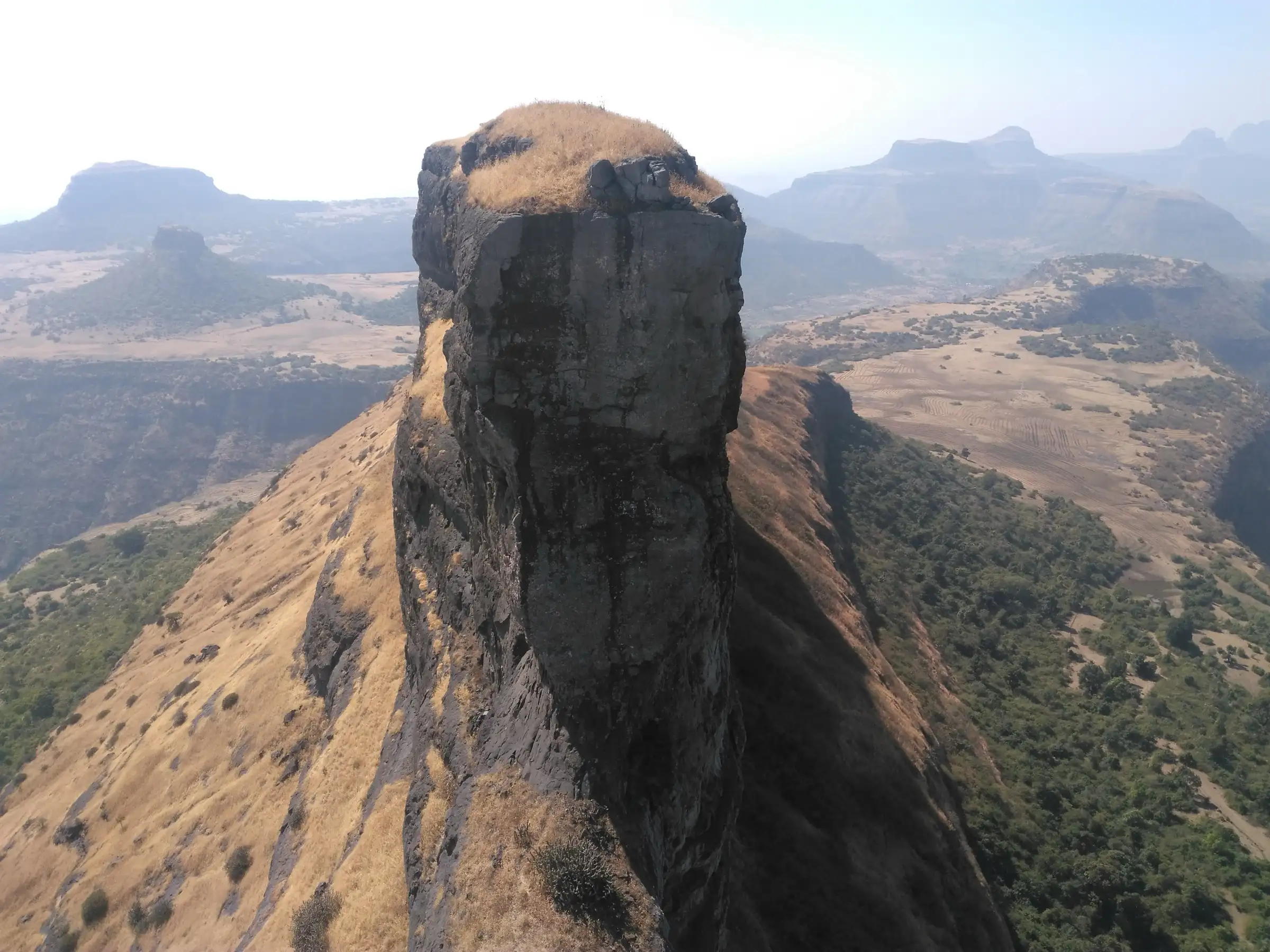 Sheer rock blade of the Dhodap cleft standing above dry grassy ridges and the Satmala hills