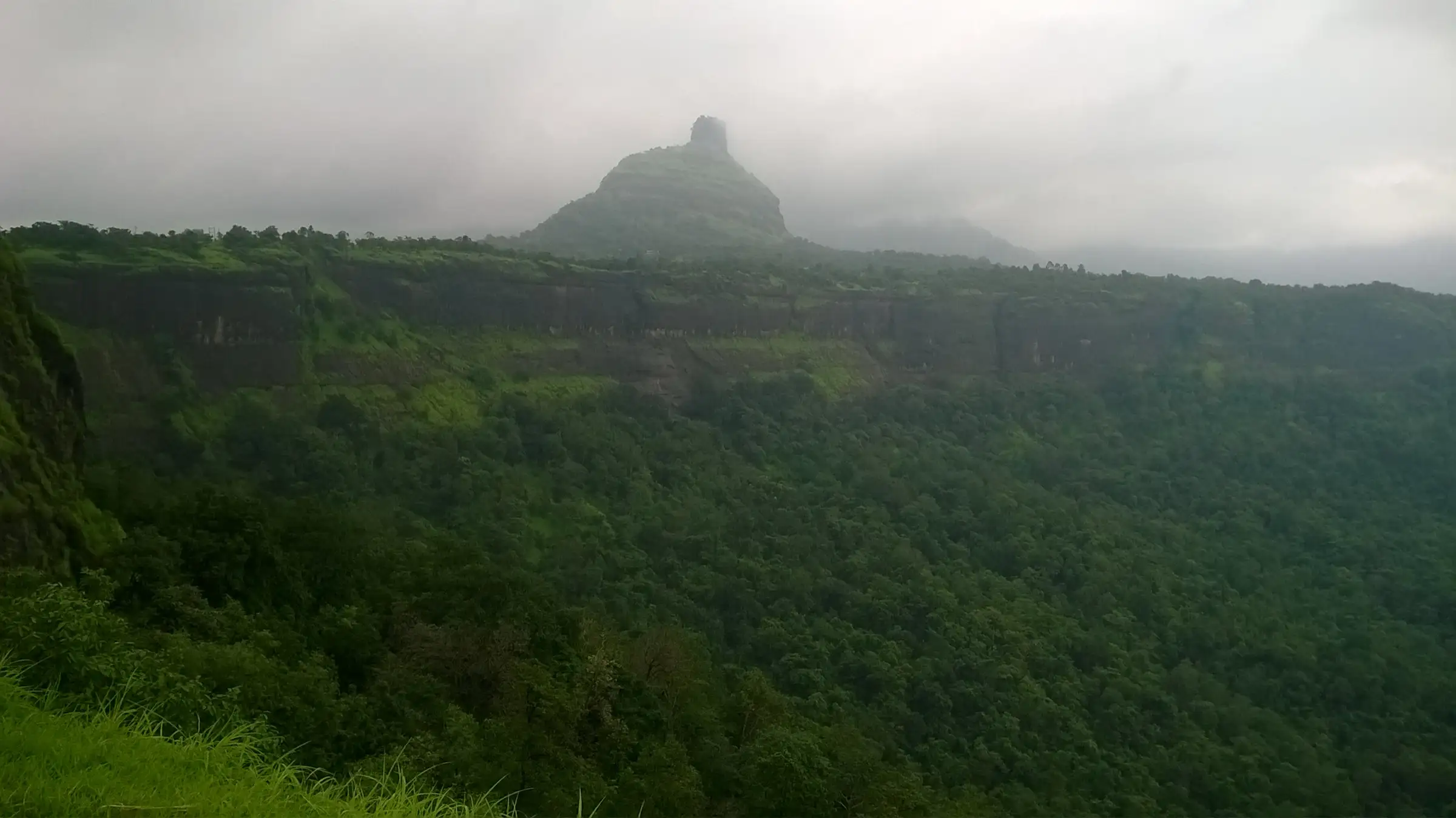 The thumb-shaped pinnacle of Kothaligad rising above the forested Peth plateau under monsoon cloud