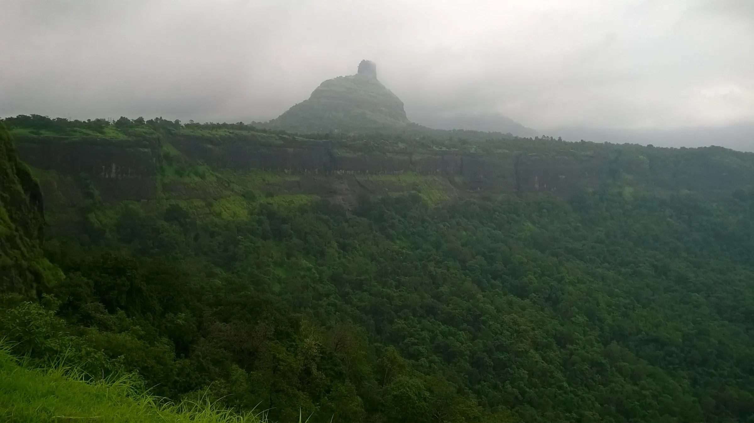 The thumb-shaped pinnacle of Kothaligad rising above the forested Peth plateau under monsoon cloud