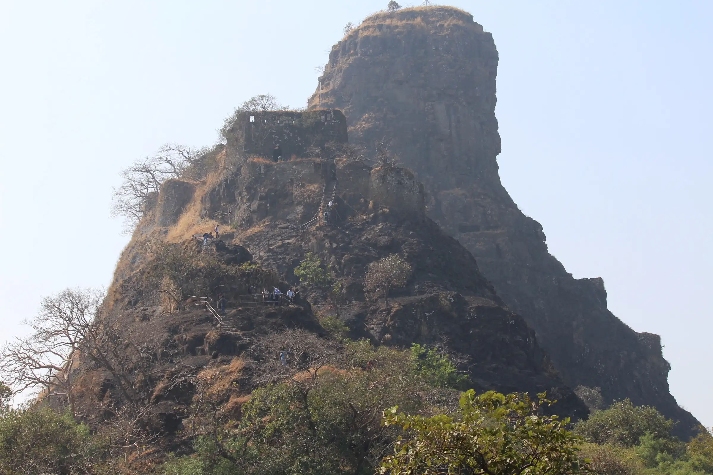 The basalt pinnacle of Karnala Fort rising behind the fort walls, with trekkers on the steps below