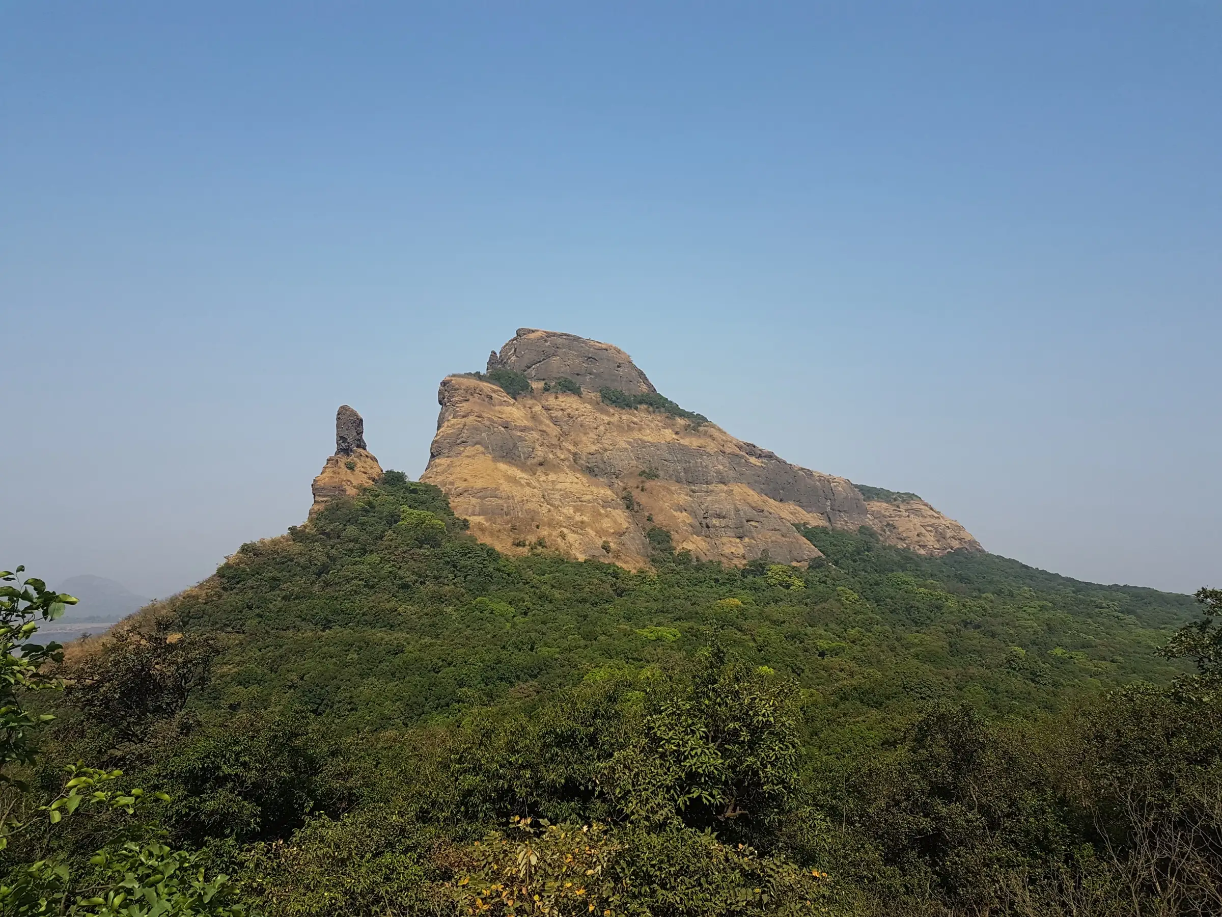 The Dhak hill and the slender Kalakrai pinnacle rising above thick green forest under a hazy blue sky