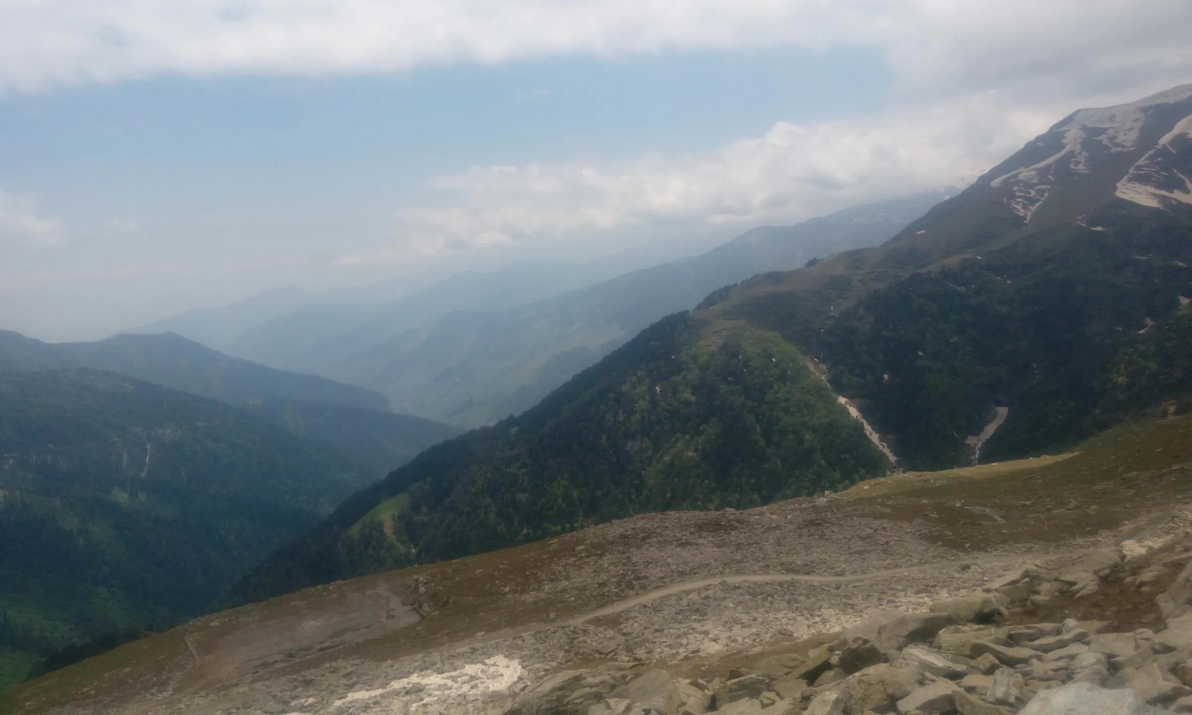 Forested ridges of the Pir Panjal falling away below a rocky slope near the top of Sach Pass
