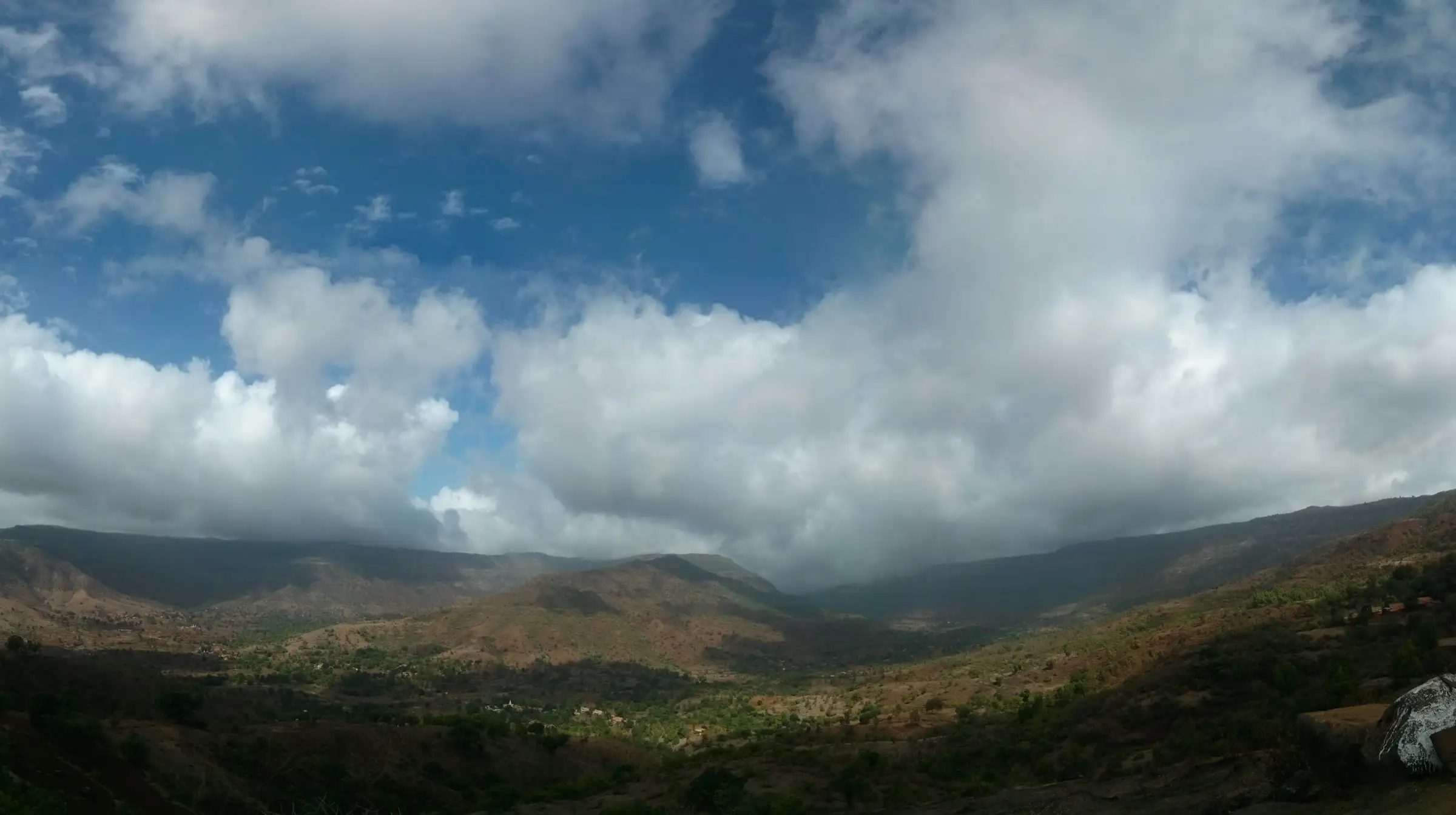 Panoramic view from Raireshwar over a green valley and flat-topped Sahyadri ridges under heavy clouds