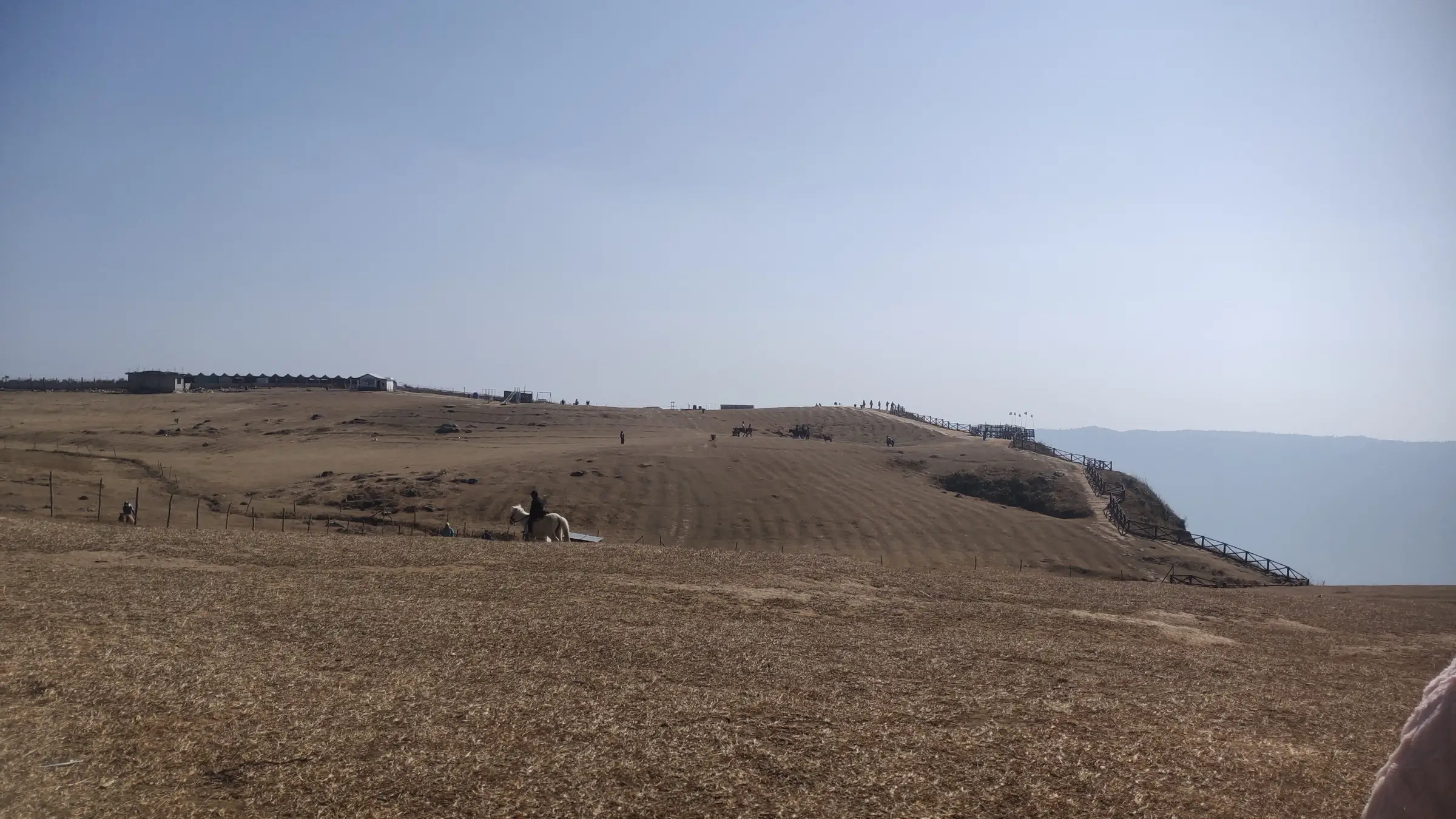 Dry golden grassland on the Laitlum plateau with a rider on a white horse and a fenced path leading to the canyon edge