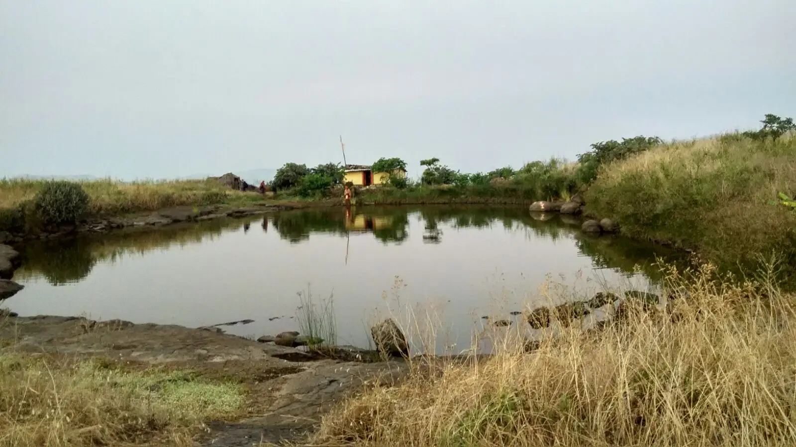 Pond on the grassy top of Kavnai Fort with a small yellow temple and flagpole on the far bank