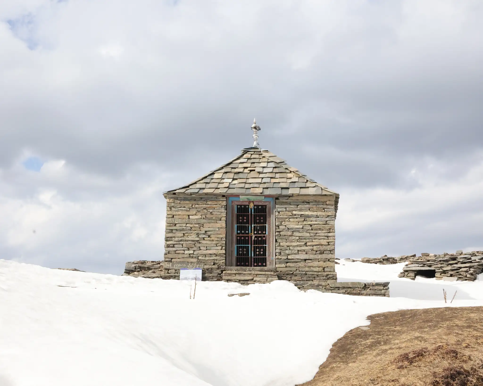 Small stone temple with a slate roof at Raghupur Fort, surrounded by spring snow